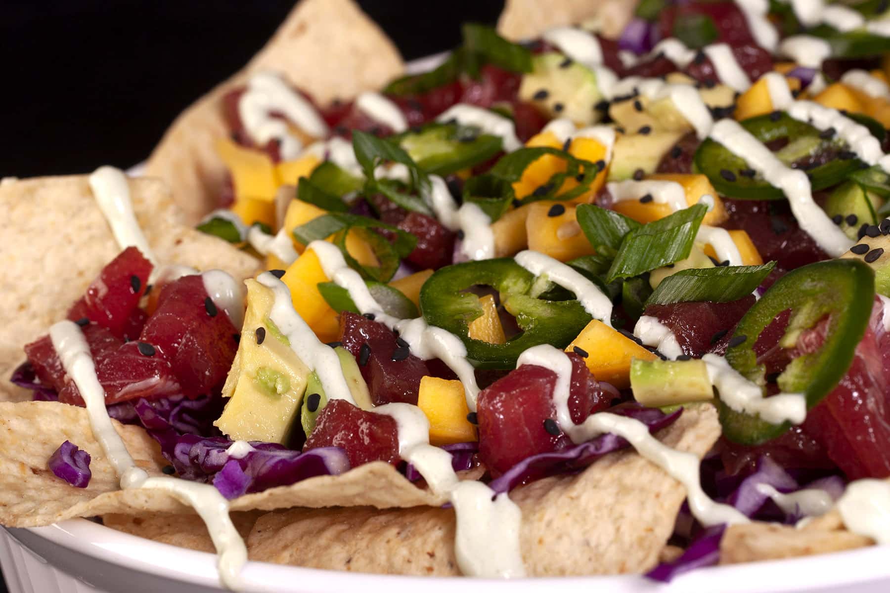 A platter of tuna poke nachos, with mango, avocado, purple cabbage, jalapeno slices, and wasabi mayo.