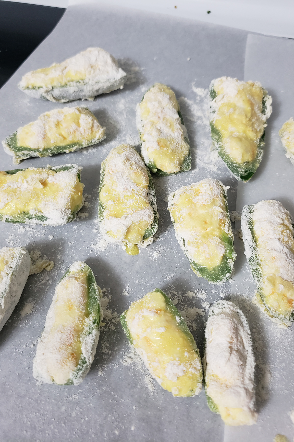A close up view of filled jalapeno halves that have been dipped in egg and flour, arranged on parchment paper.