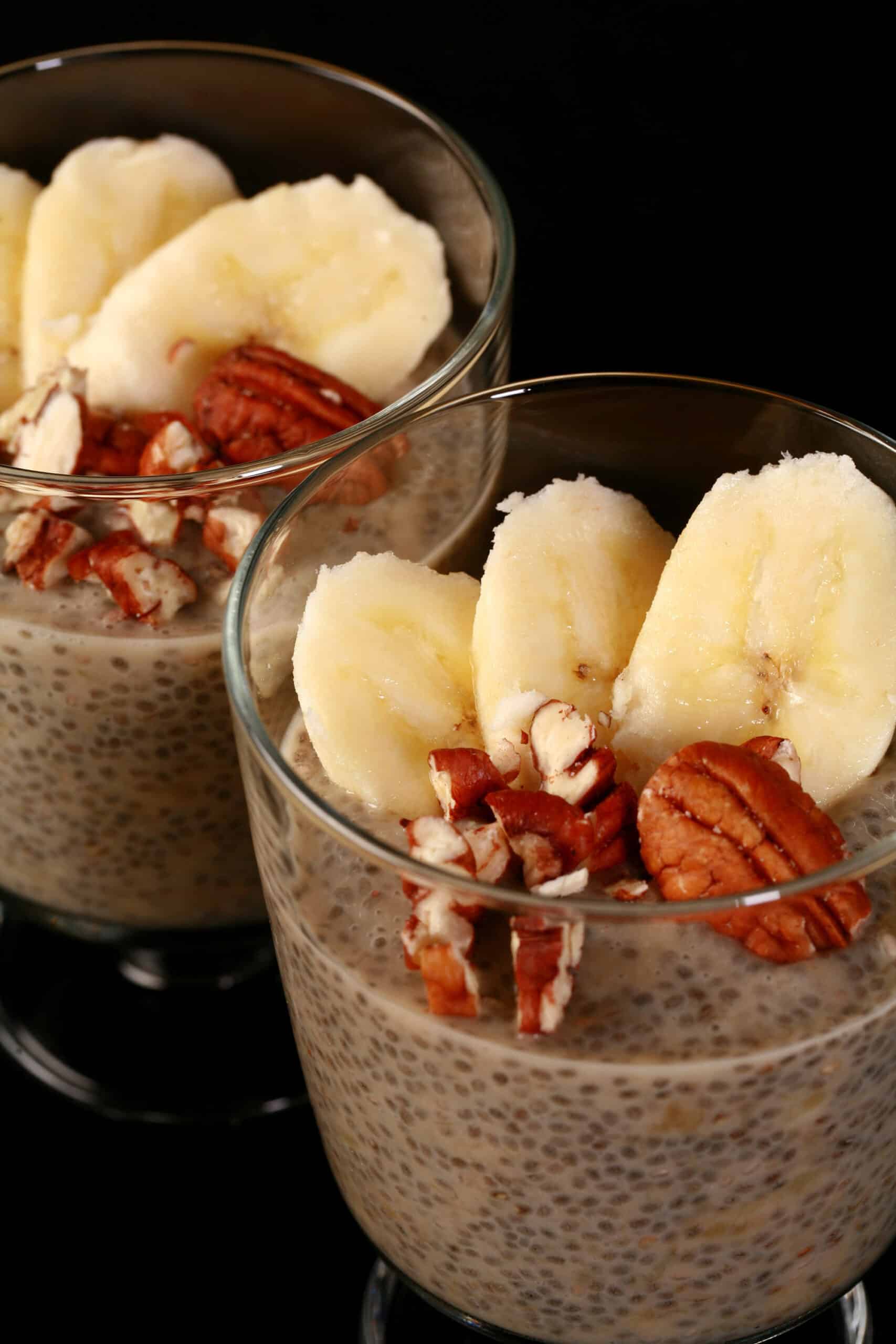 2 serving glasses of banana chia pudding, topped with banana slices and pecans.