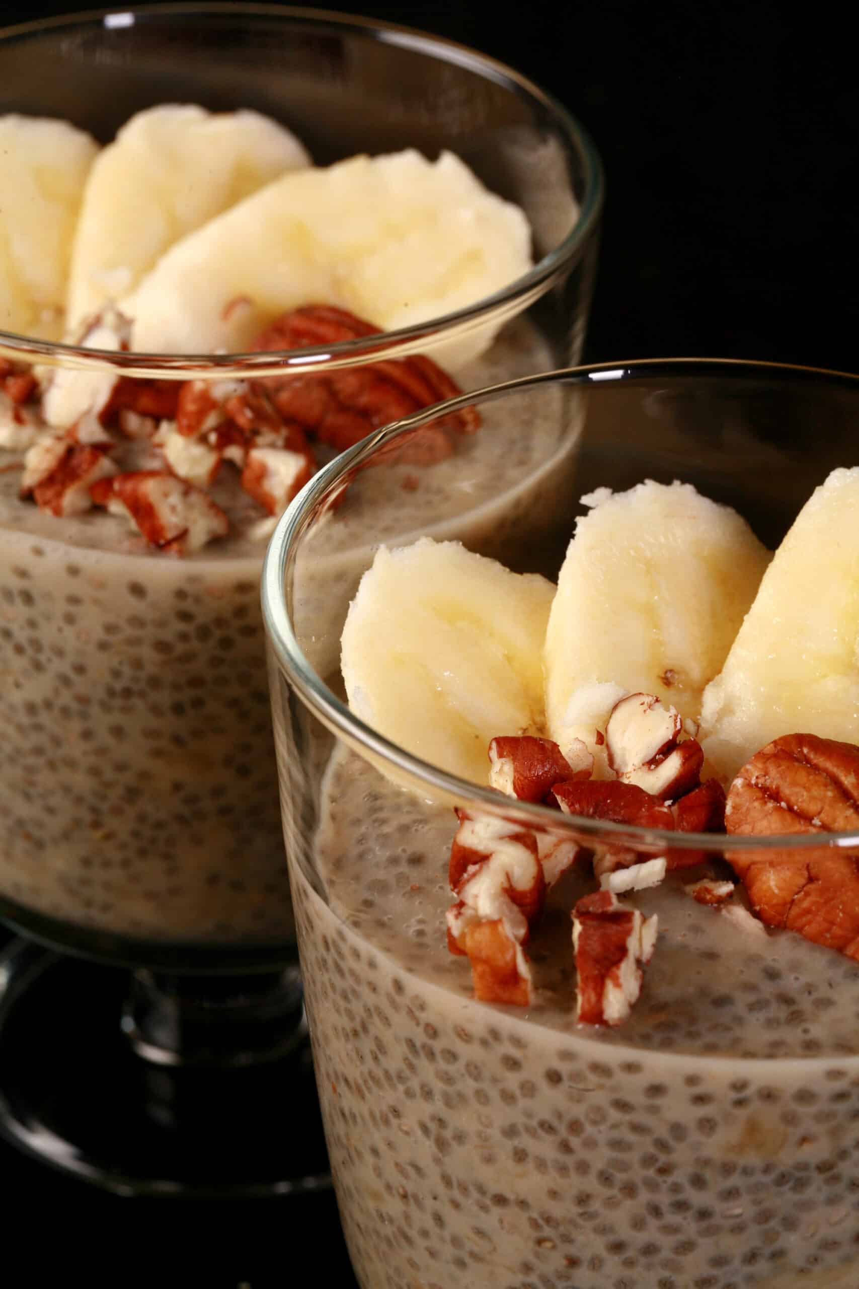 2 serving glasses of banana chia pudding, topped with banana slices and pecans.