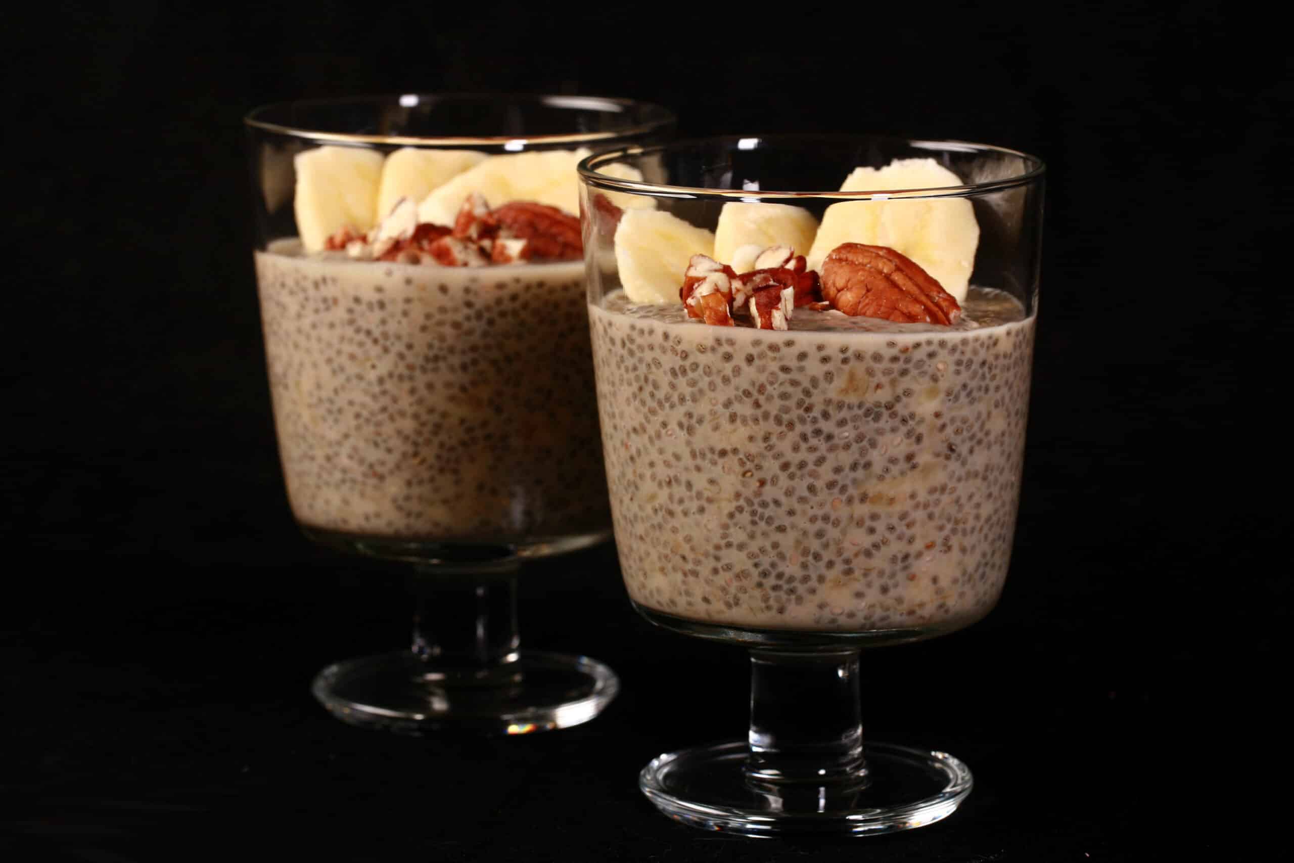 2 serving glasses of banana chia pudding, topped with banana slices and pecans.