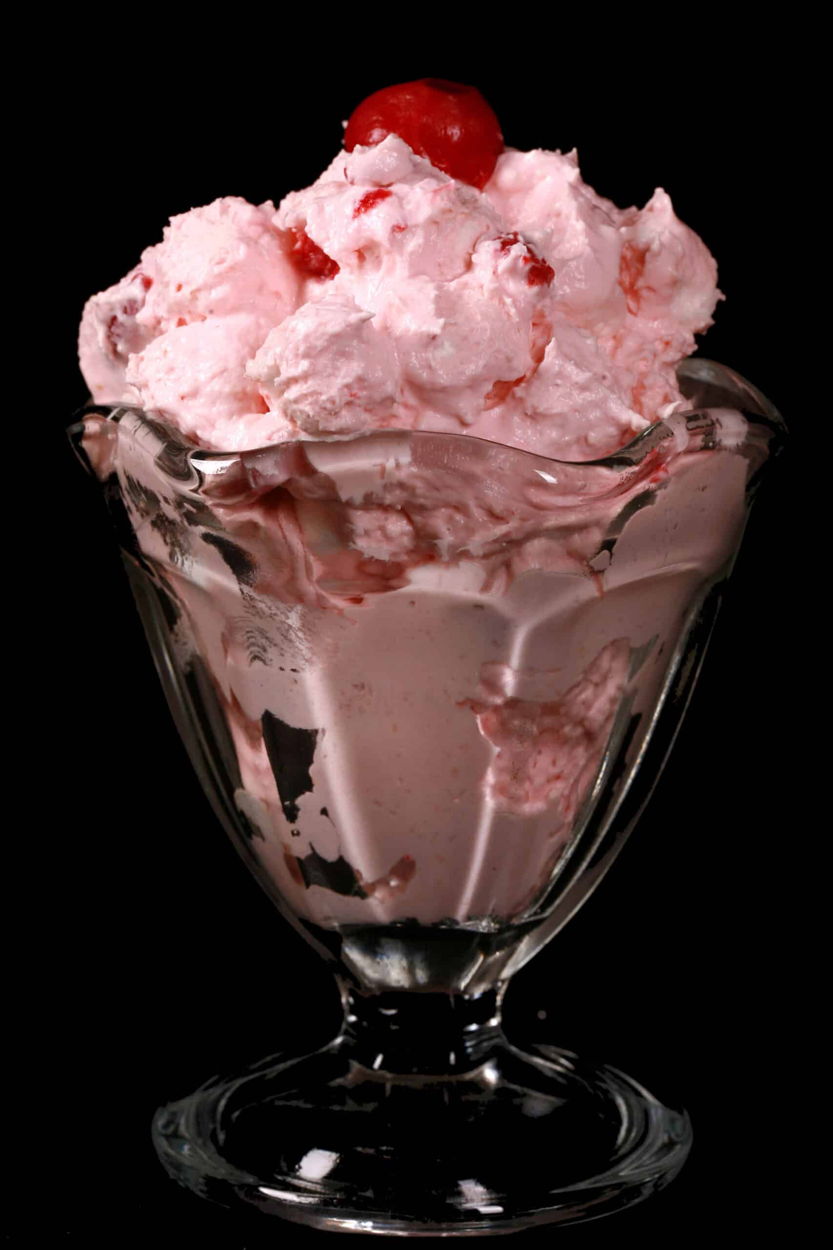 A glass serving bowl of bright pink cherry cheesecake fluff salad.