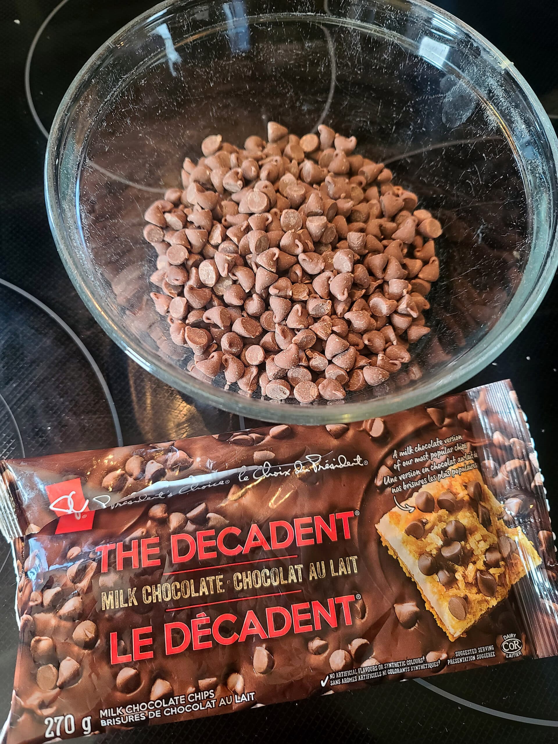 A bowl of milk chocolate chips next to a bag of chocolate chips.