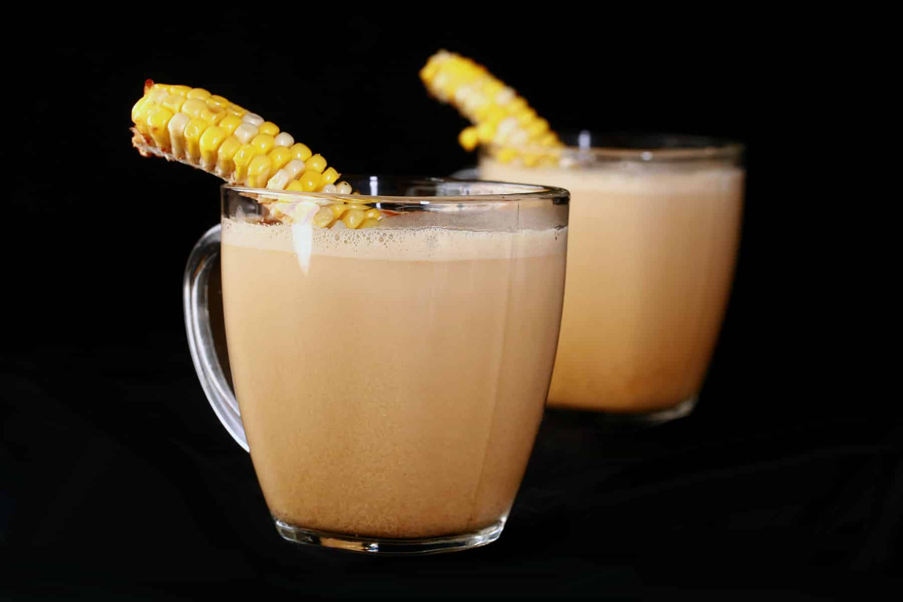 2 glass mugs of con cappuccino, garnished with narrow lengths of corn on the cob.