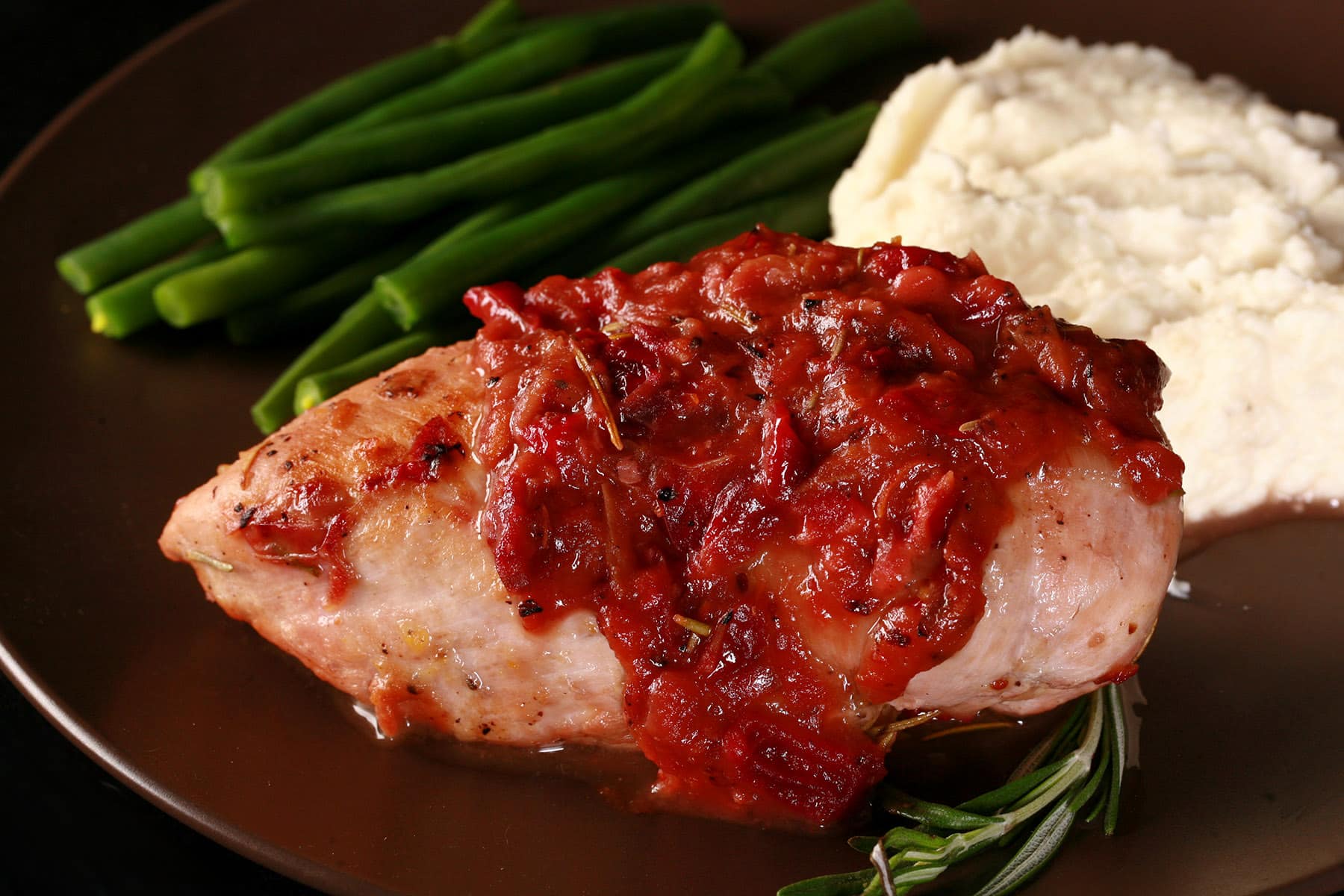 A serving of cranberry chicken on a plate with green beans and mashed cauliflower.