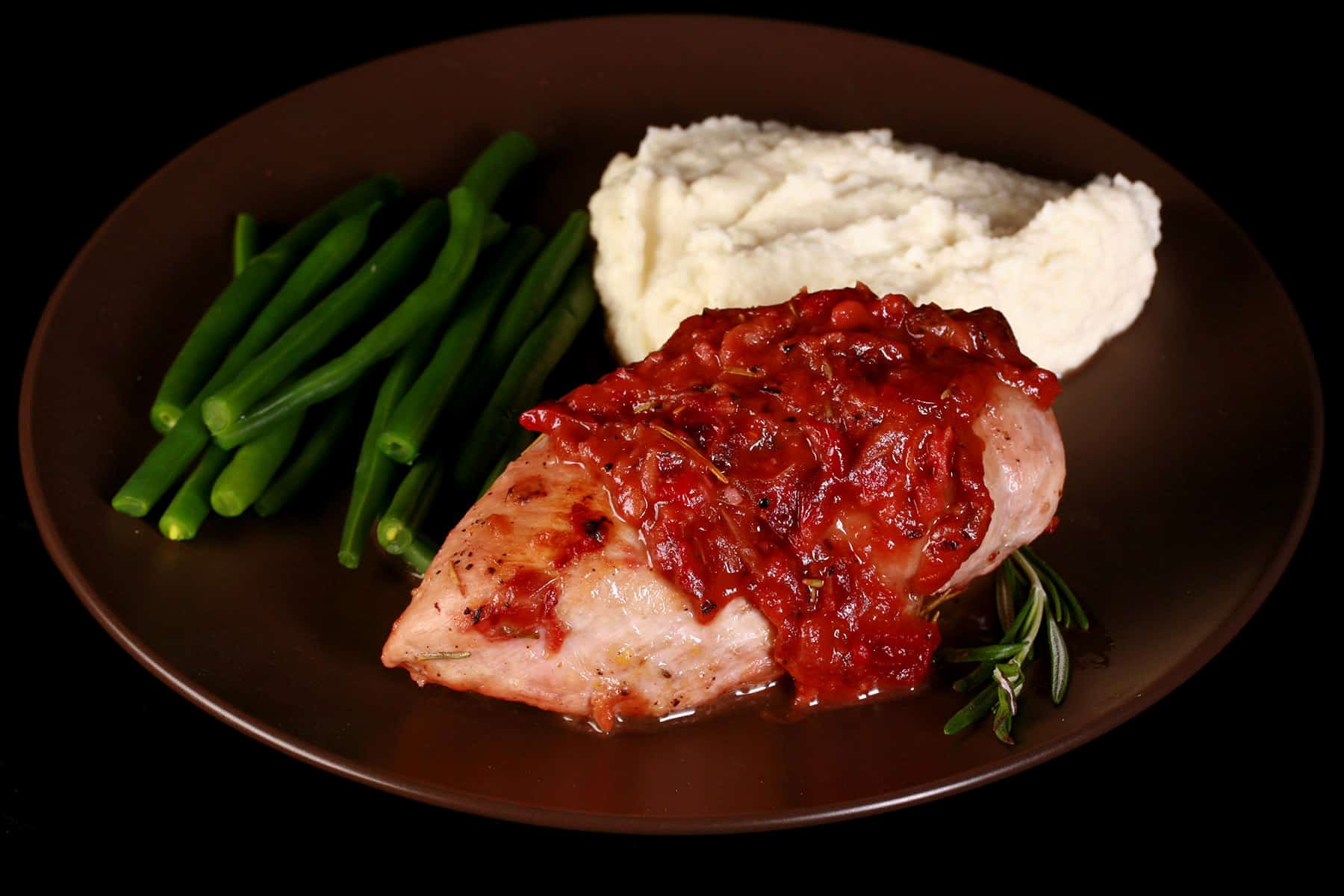 A serving of cranberry chicken on a plate with green beans and mashed cauliflower.