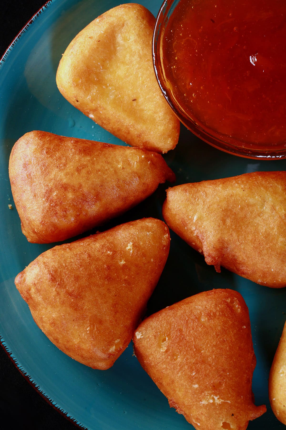 A plate of battered, deep fried brie cheese wedges, around a bowl of apricot preserves.