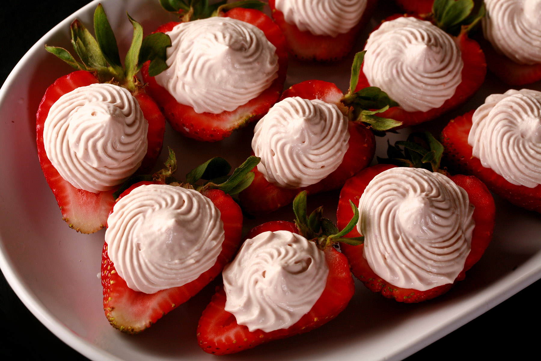 A white plate with deviled strawberries, filled with a cream cheese and balsamic vinegar whipped cream.