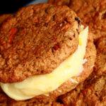 A small blue and white plate with a stack of gluten-free carrot cake cookies on it. The filling is ivory coloured and has flecks of orange zest throughout