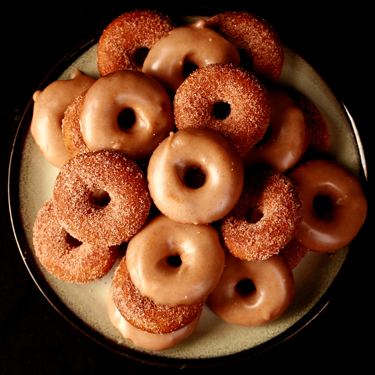 Close up view of gluten-free pumpkin spice mini doughnuts. Some are coated in cinnamon sugar, others are glazed with a tan coloured frosting