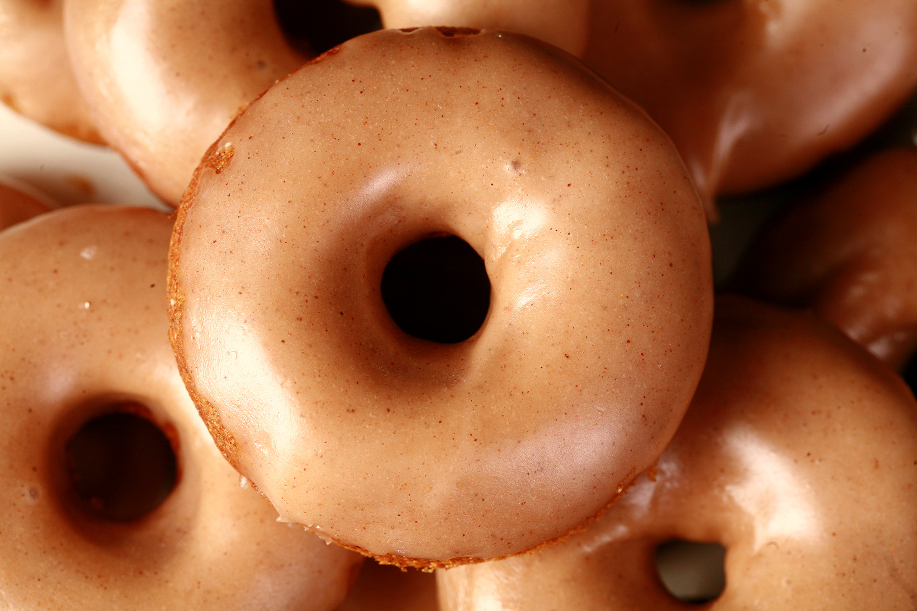 Close up view of gluten-free pumpkin spice mini doughnuts. They are glazed with a tan coloured maple frosting.