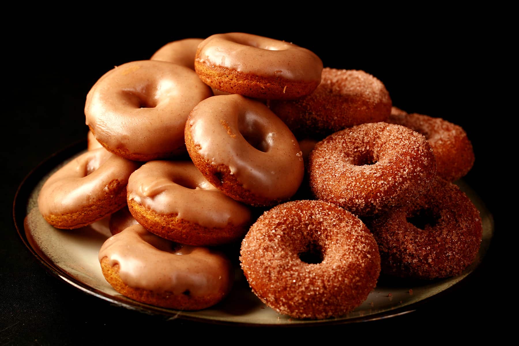 Close up view of gluten-free pumpkin spice mini doughnuts. Some are coated in cinnamon sugar, others are glazed with a tan coloured frosting.