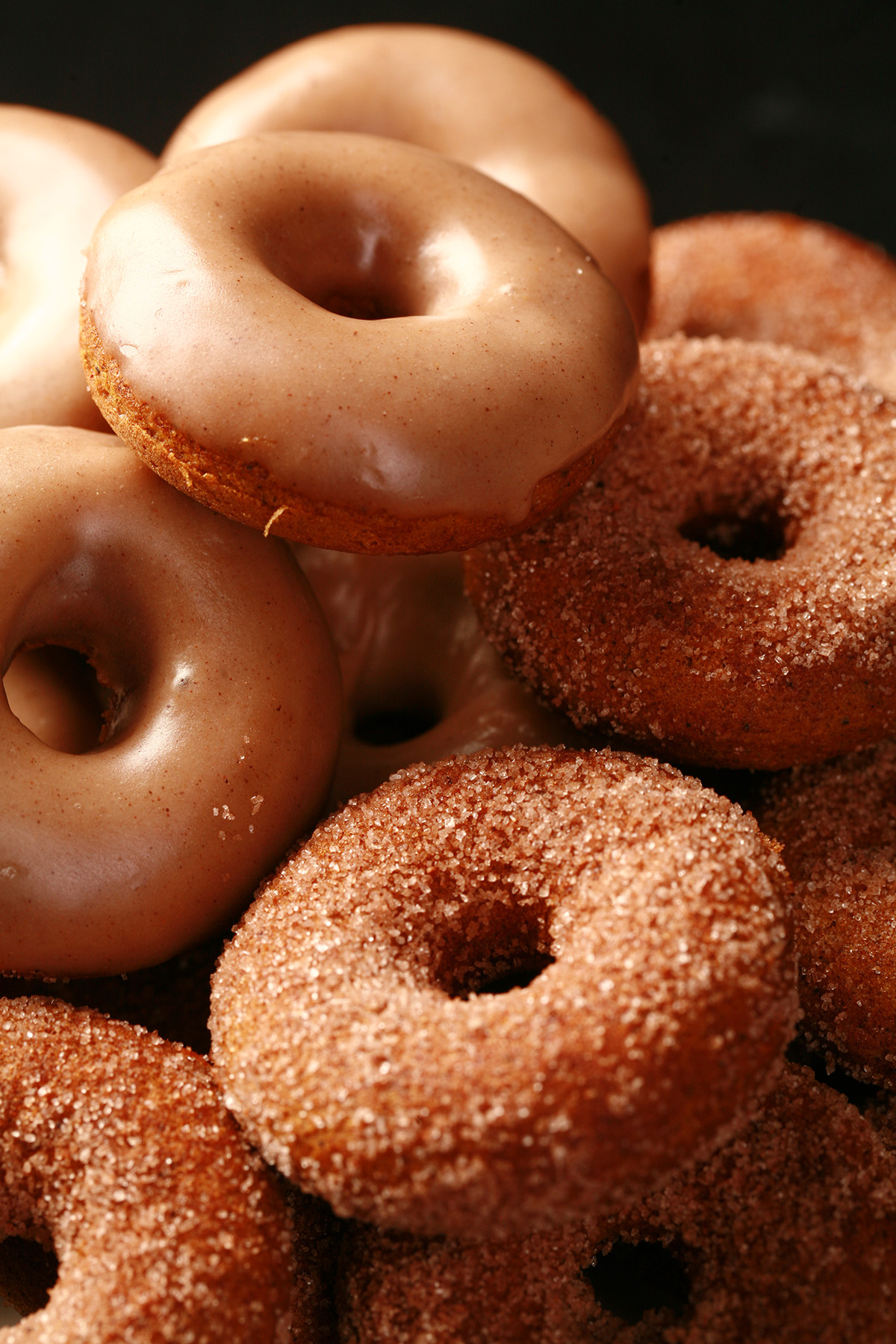 Close up view of gluten-free pumpkin spice mini doughnuts. Some are coated in cinnamon sugar, others are glazed with a tan coloured frosting