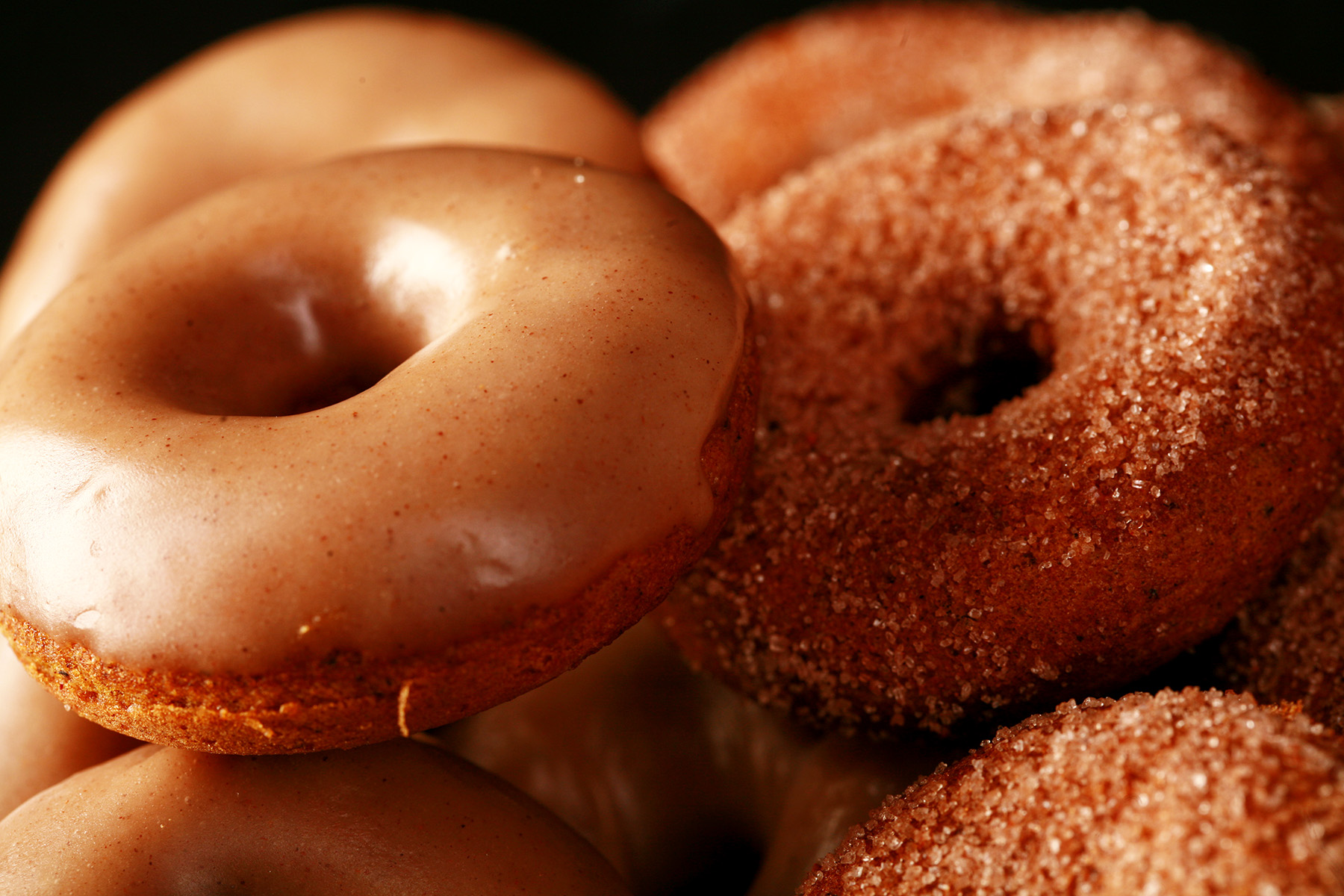 Close up view of gluten-free pumpkin spice mini doughnuts. Some are coated in cinnamon sugar, others are glazed with a tan coloured frosting