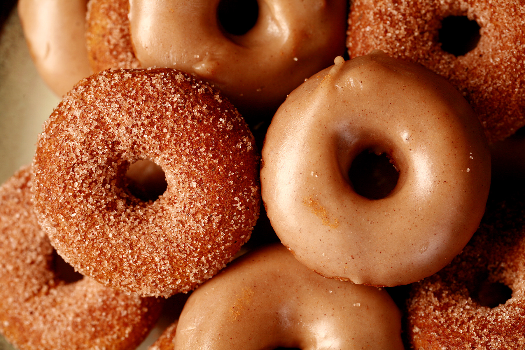 Close up view of gluten-free pumpkin spice mini doughnuts. Some are coated in cinnamon sugar, others are glazed with a tan coloured frosting