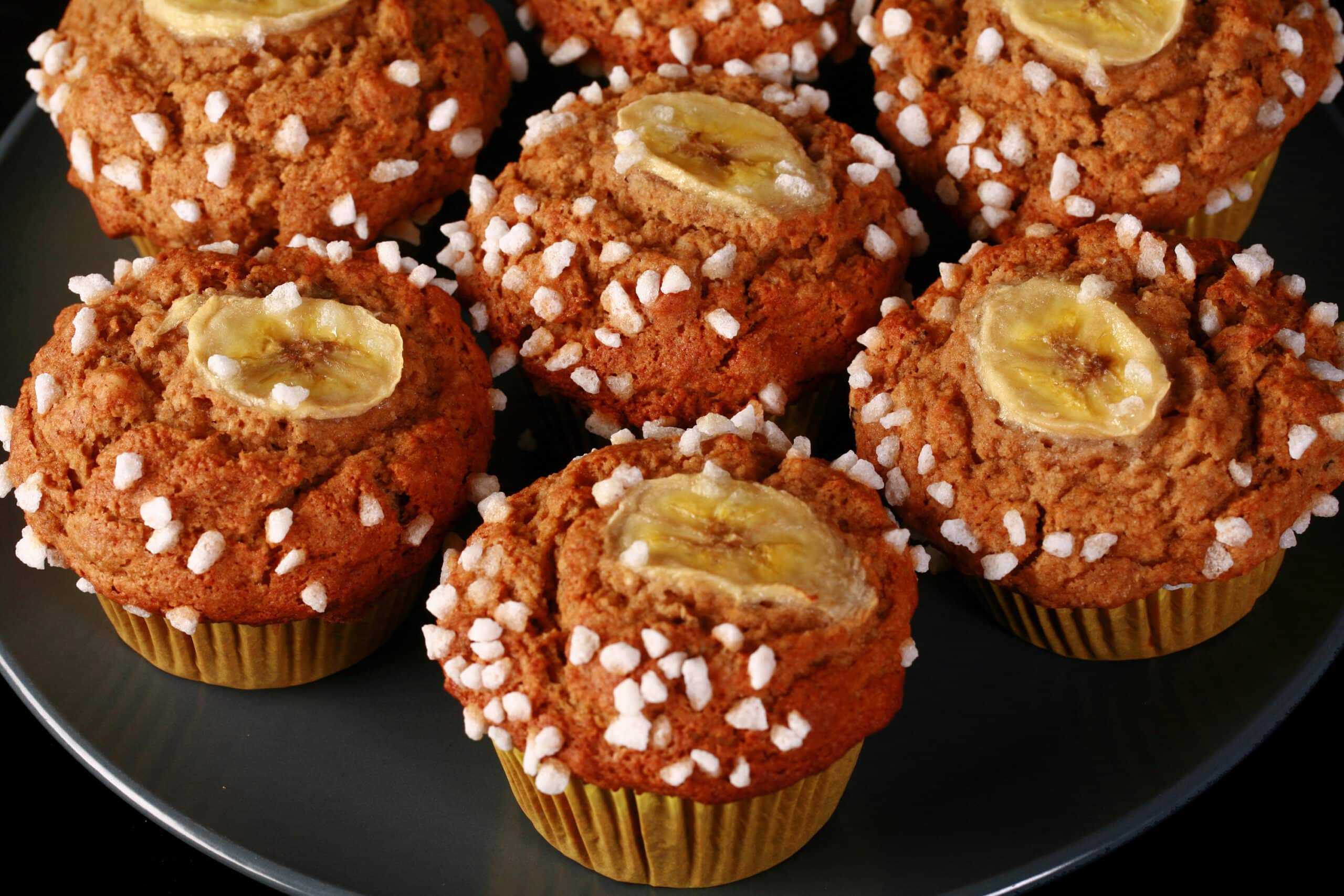 A plate of gluten-free banana muffins, topped with coarse sugar and banana slices.