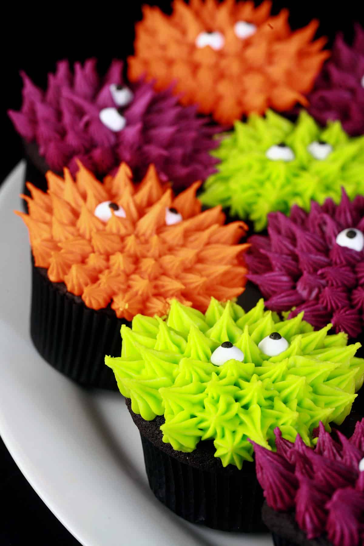 Several brightly coloured monster themed halloween cupcakes, made on gluten-free black velvet cupcakes.