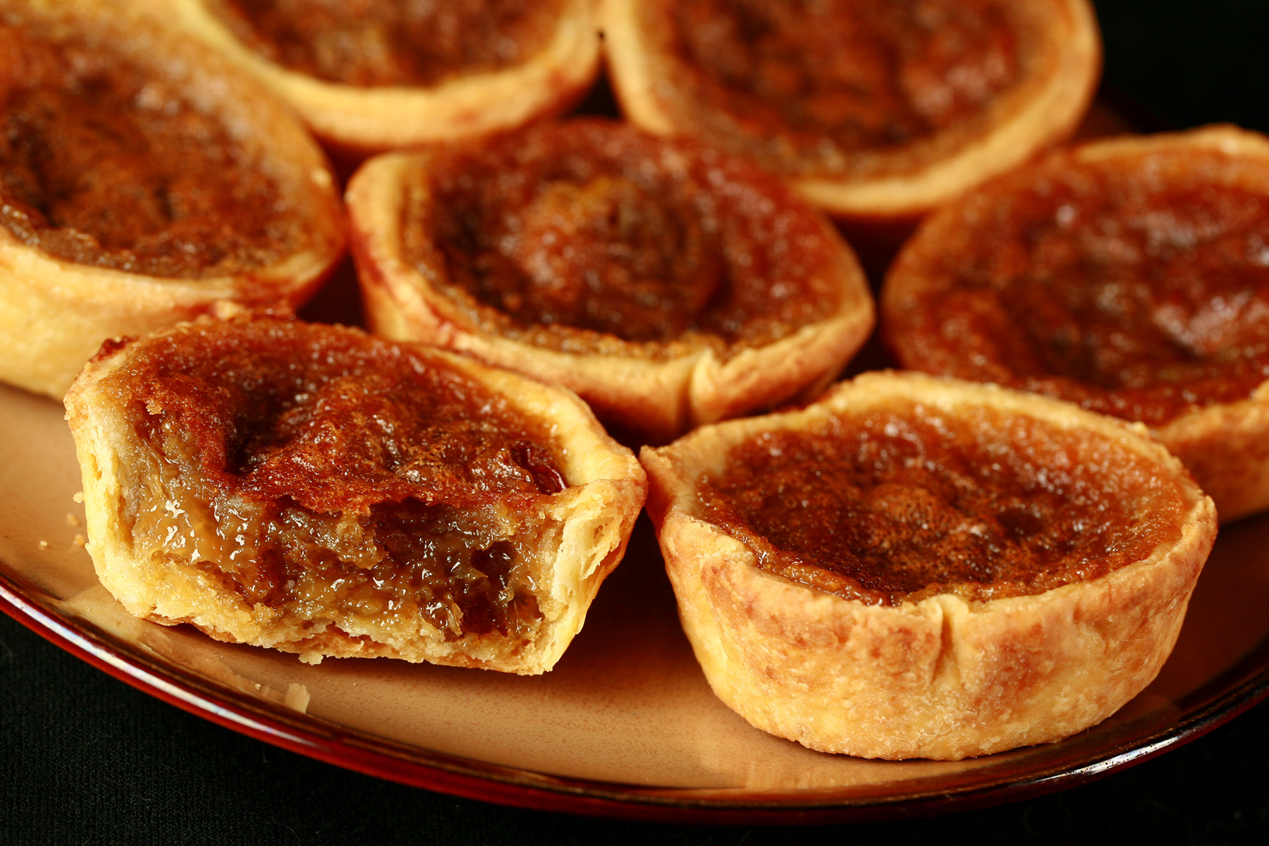 A brown plate is crowded with gluten-free buttertarts - mini tarts with a gooey sugar filling and raisins.