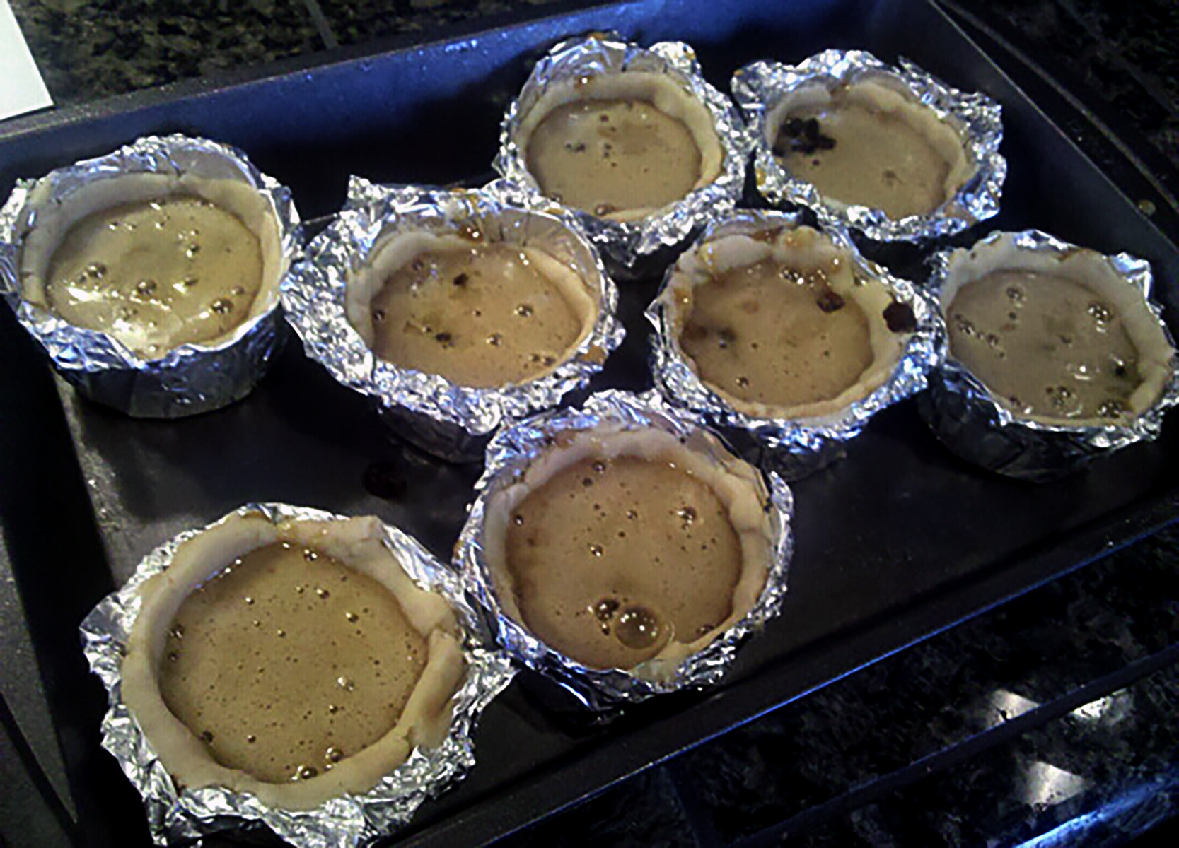 Homemade foil cuts, arranged in baking pans. The cups have been lined with dough and filled with raisings and filling.