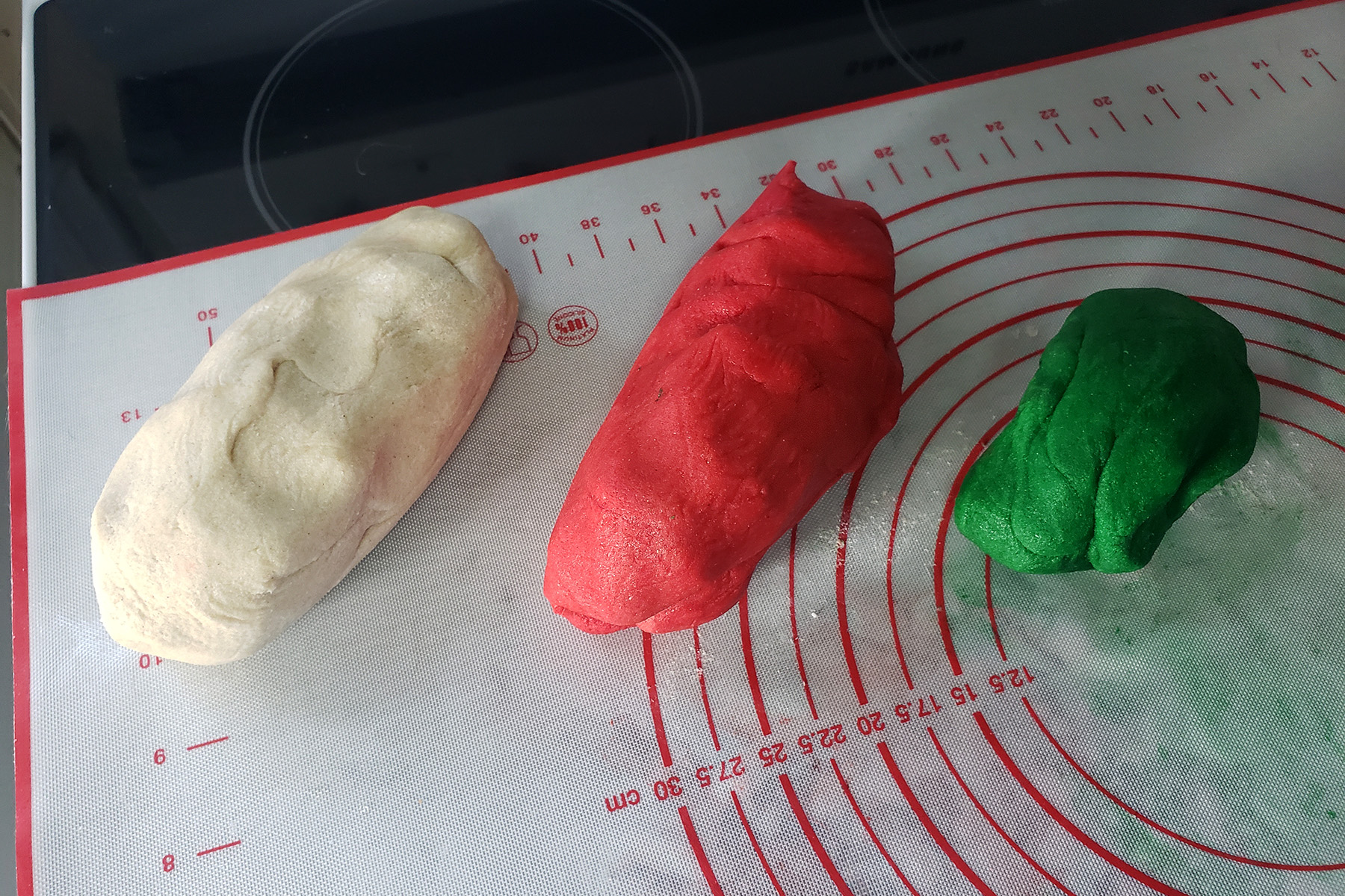 Lumps of white, red, and green dough rest on a silicone baking mat.