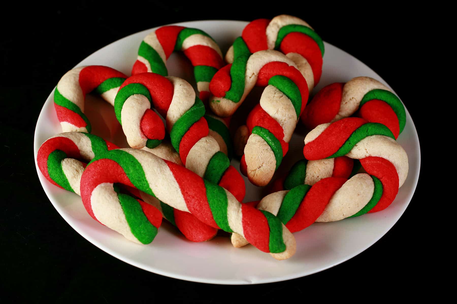 Gluten-Free Candy Cane cookies - candy cane shaped cookies, made from lengths of red, green, and white twisted dough - on a plate.