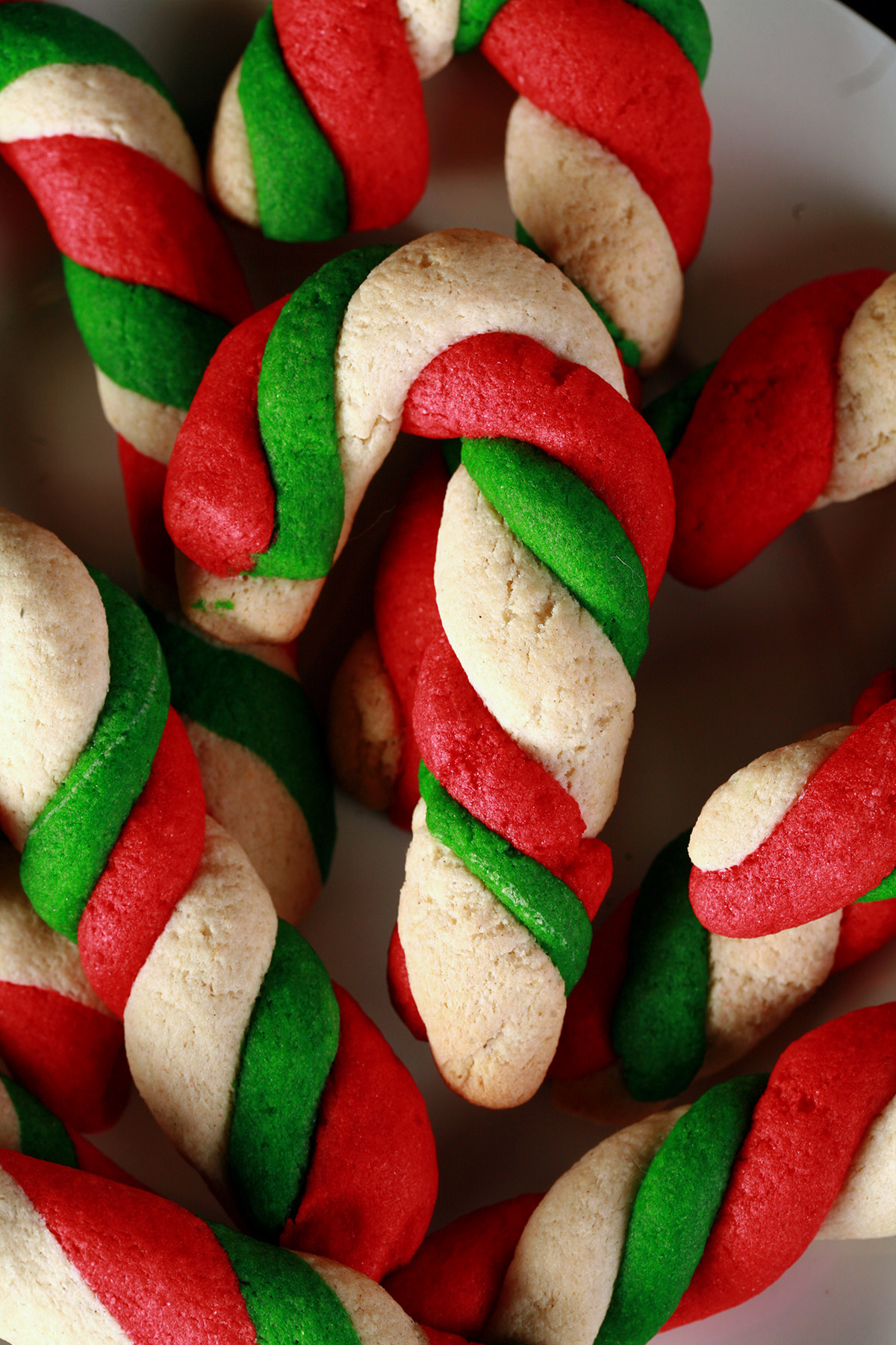 Gluten-Free Candy Cane cookies - candy cane shaped cookies, made from lengths of red, green, and white twisted dough - on a plate.