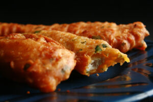 Several strips of gluten-free chicken pakora on a blue plate. They are golden deep fried, with flecks of green cilantro.