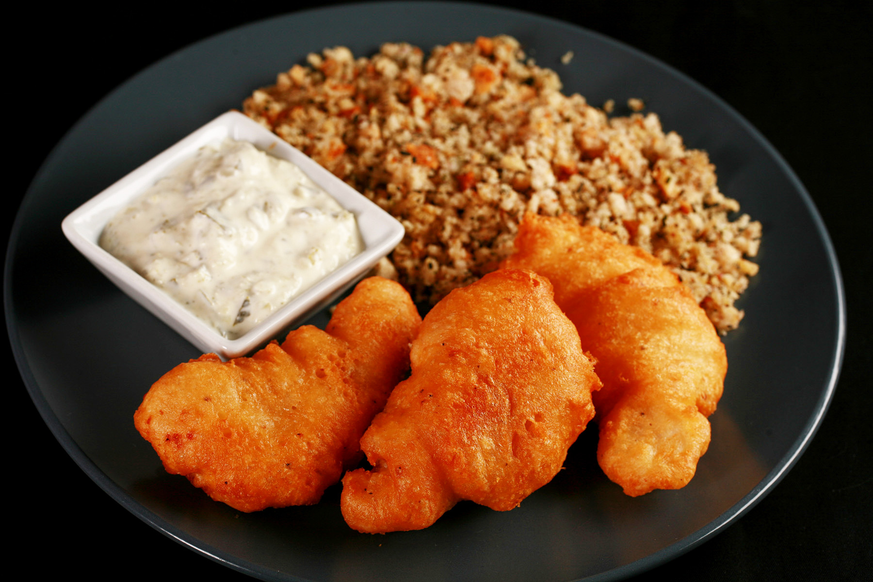 Gluten-Free Cod Cheeks and Dressing, on a round, blue plate. There is a small dish of tartar sauce on the plate, as well.
