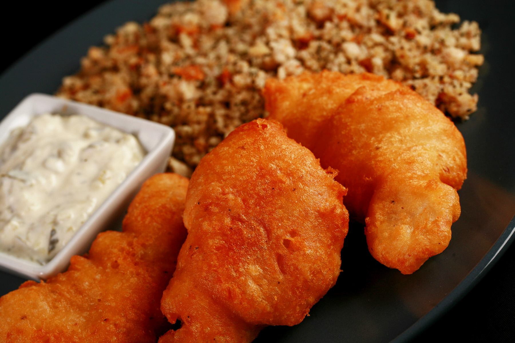 Gluten-Free Cod Cheeks and gluten-free Dressing, on a round, blue plate. There is a small dish of tartar sauce on the plate, as well.