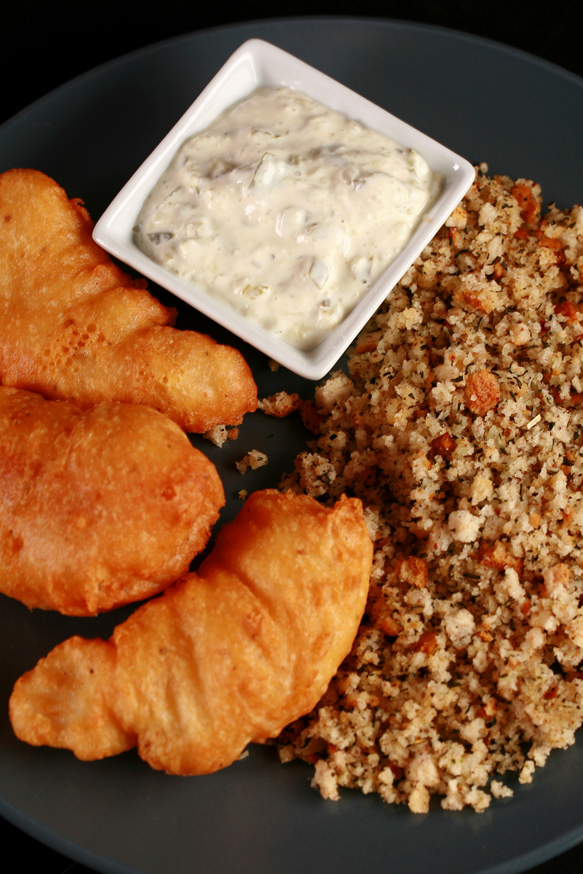 Gluten-Free Cod Cheeks and Dressing, on a round, blue plate. There is a small dish of tartar sauce on the plate, as well.