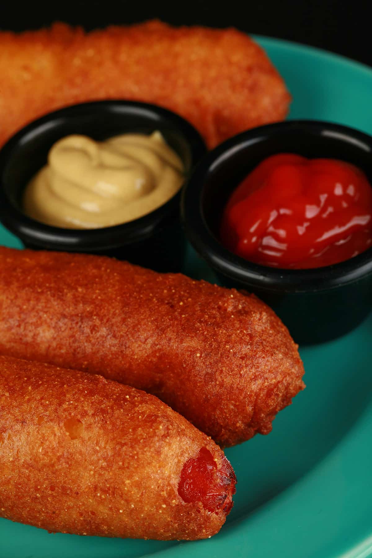 3 gluten free corn dogs on a plate with mustard and ketchup.