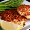 2 Gluten-free Crab Cakes on a plate with asparagus, a lemon slice, and some fresh dill.