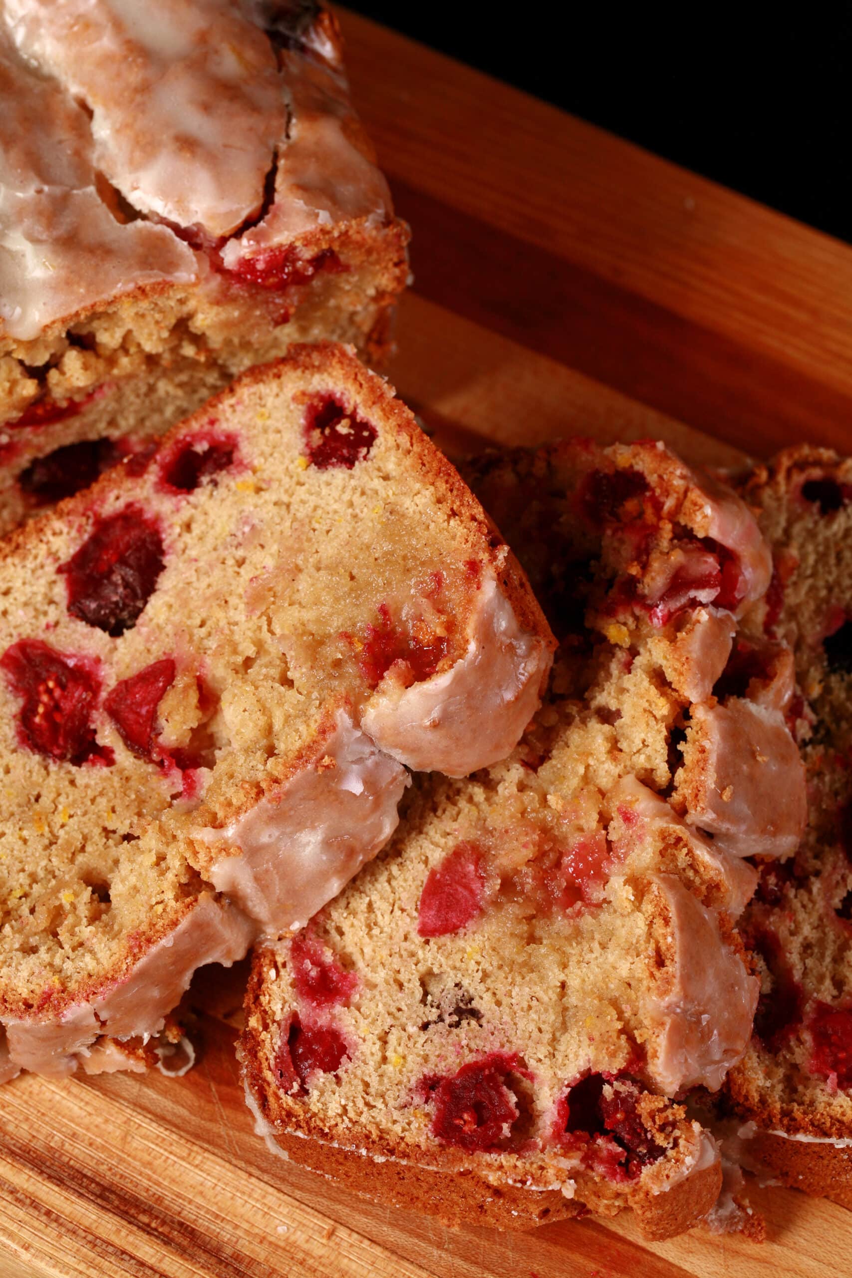A loaf of glazed gluten-free cranberry orange bread, sliced on a cutting board.