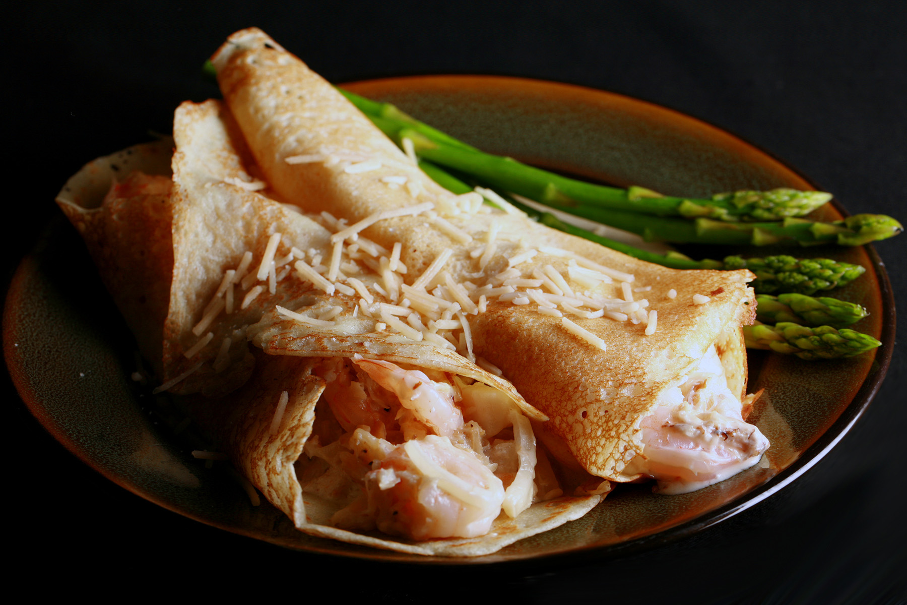 2 Gluten free seafood crepes with asparagus spears on the side.