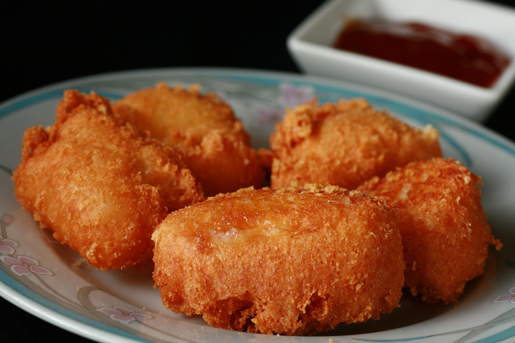 Several small wedges of gluten-free deep fried brie. There is a small bowl of apricot preserves next to the plate.