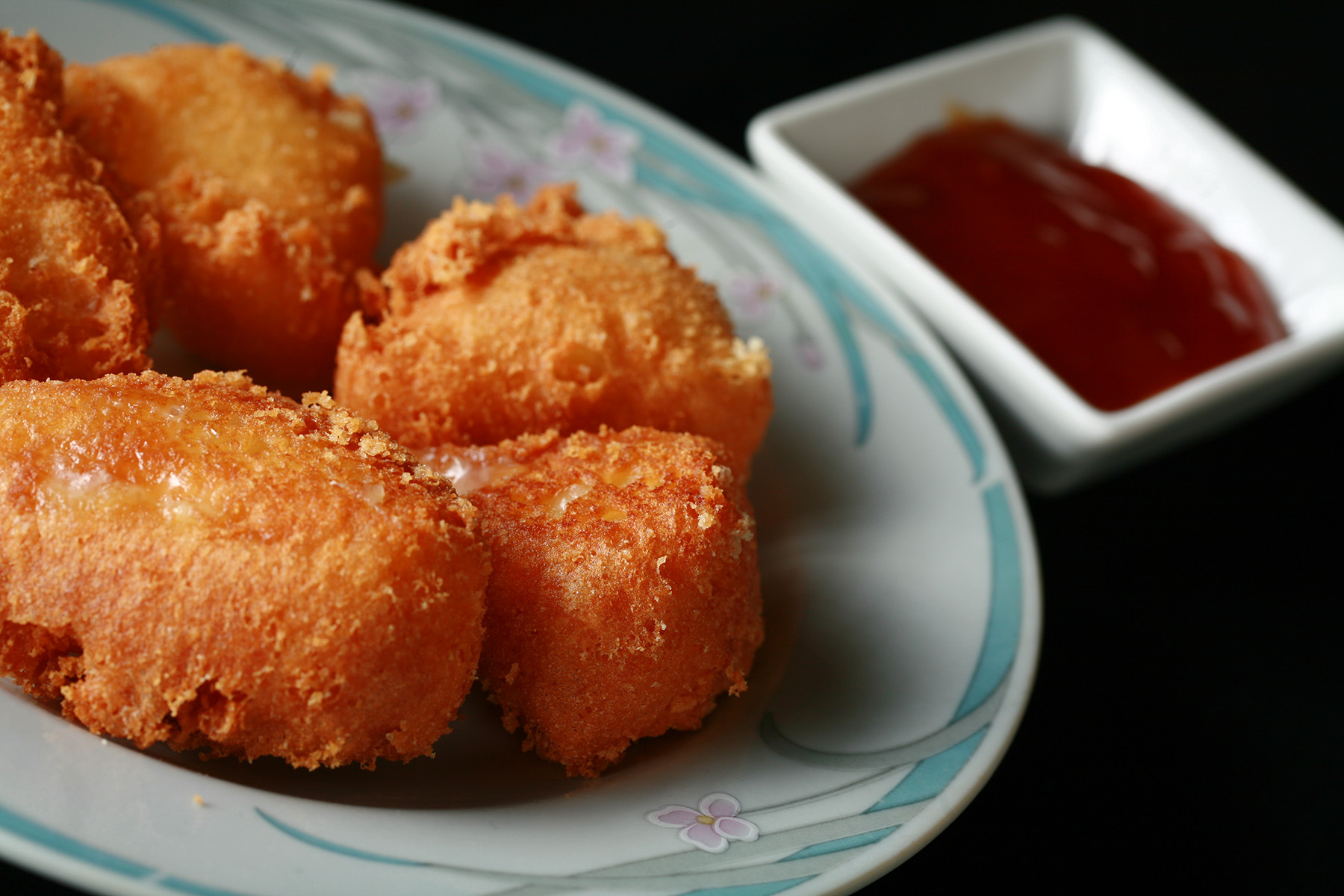 Several small wedges of gluten-free deep fried brie. There is a small bowl of apricot preserves next to the plate.