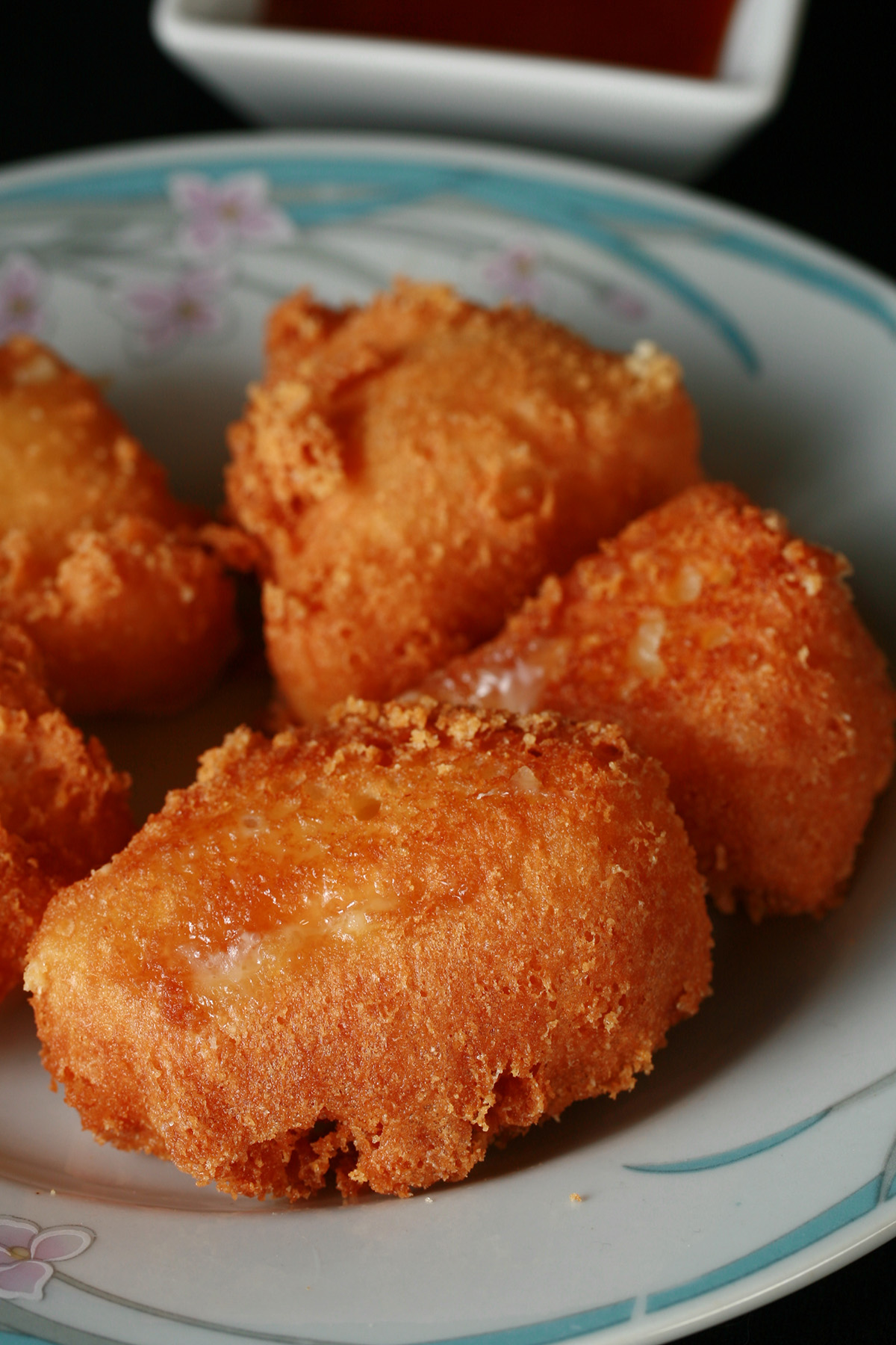 Several small wedges of gluten-free deep fried brie. There is a small bowl of apricot preserves next to the plate.