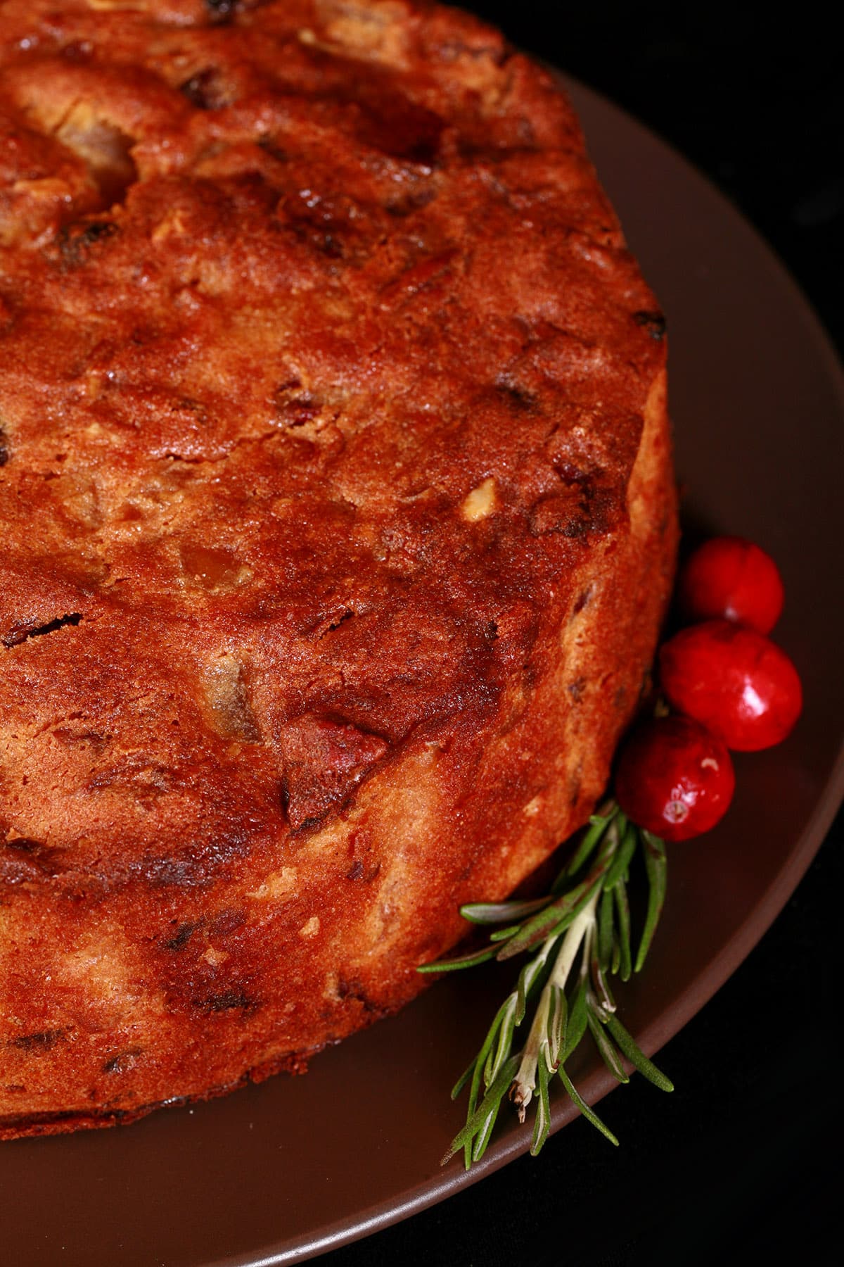 A whole gluten free fruitcake, with rosemary and cranberries beside it.