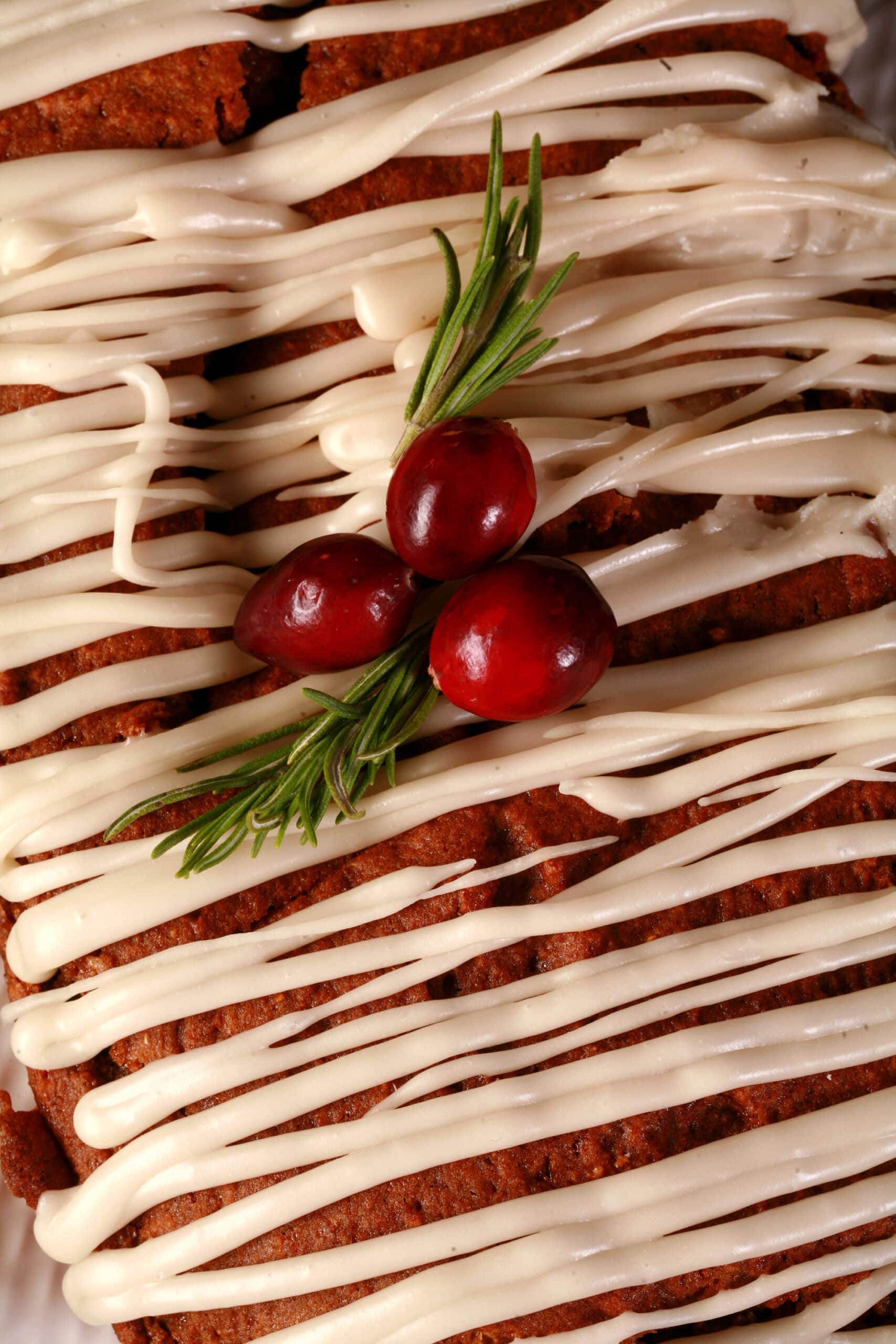 A loaf of gluten free gingerbread loaf, drizzled with vanilla glaze and garnished with rosemary and cranberries.