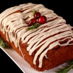 A loaf of gluten free gingerbread loaf, drizzled with vanilla glaze and garnished with rosemary and cranberries.