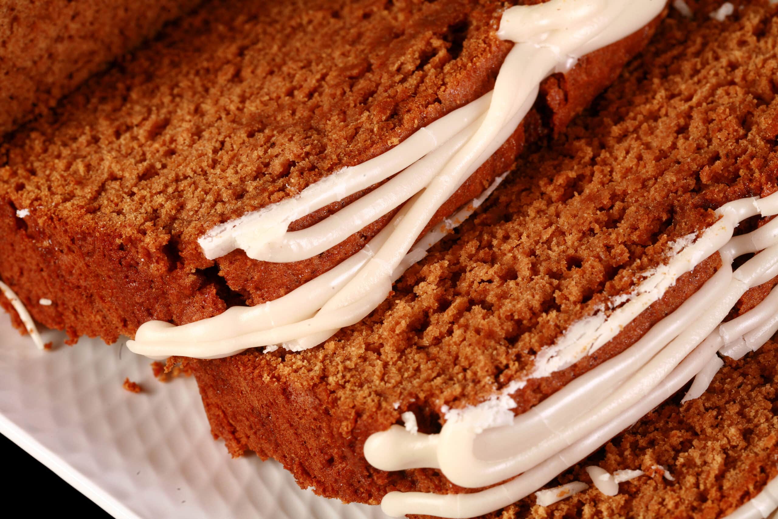 A sliced loaf of gluten-free gingerbread loaf, drizzled with vanilla glaze and garnished with rosemary and cranberries.