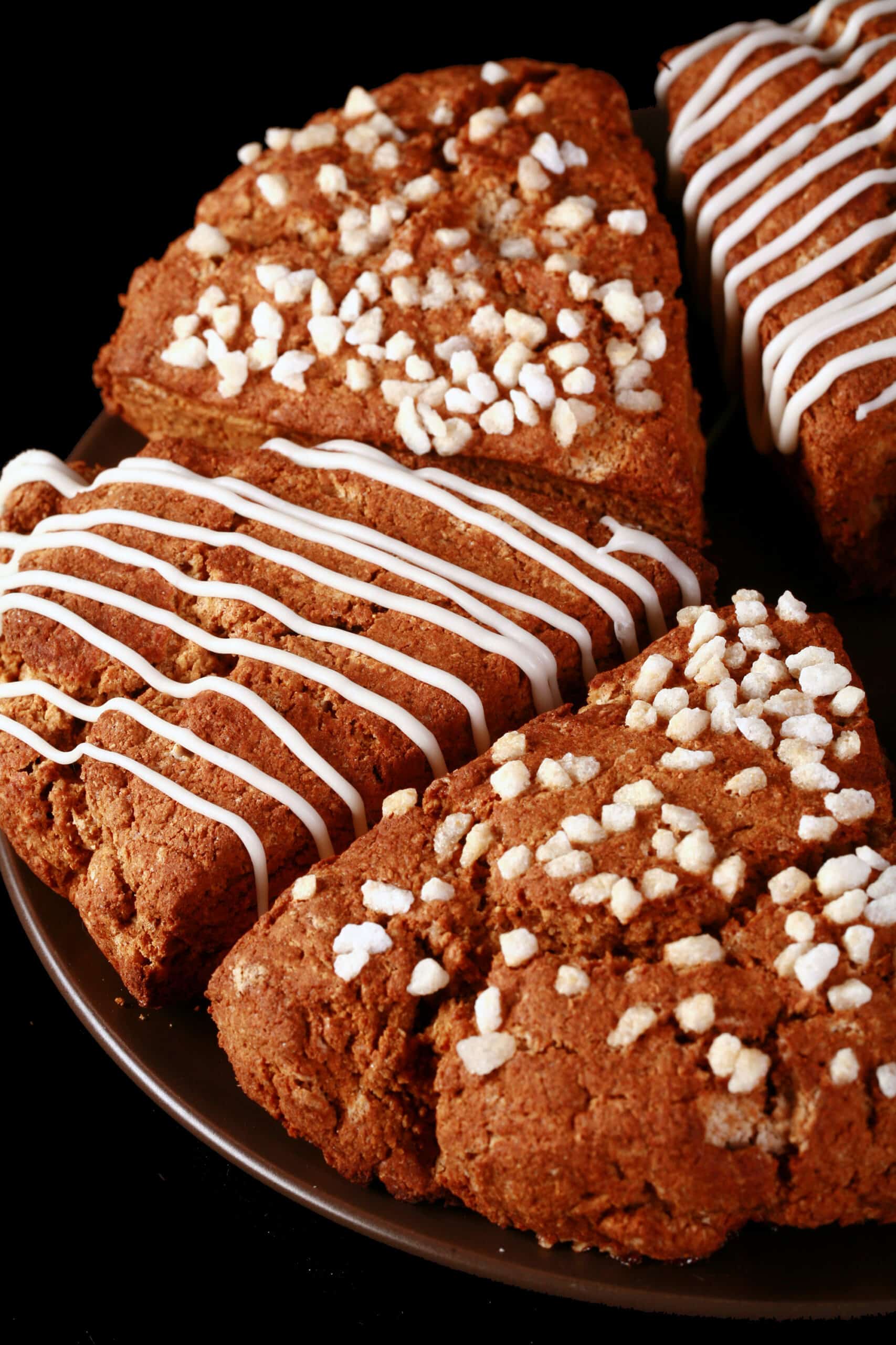 A plate of gluten free gingerbread scones. Half have a sugar crust, the other half have a vanilla glaze drizzled over them.