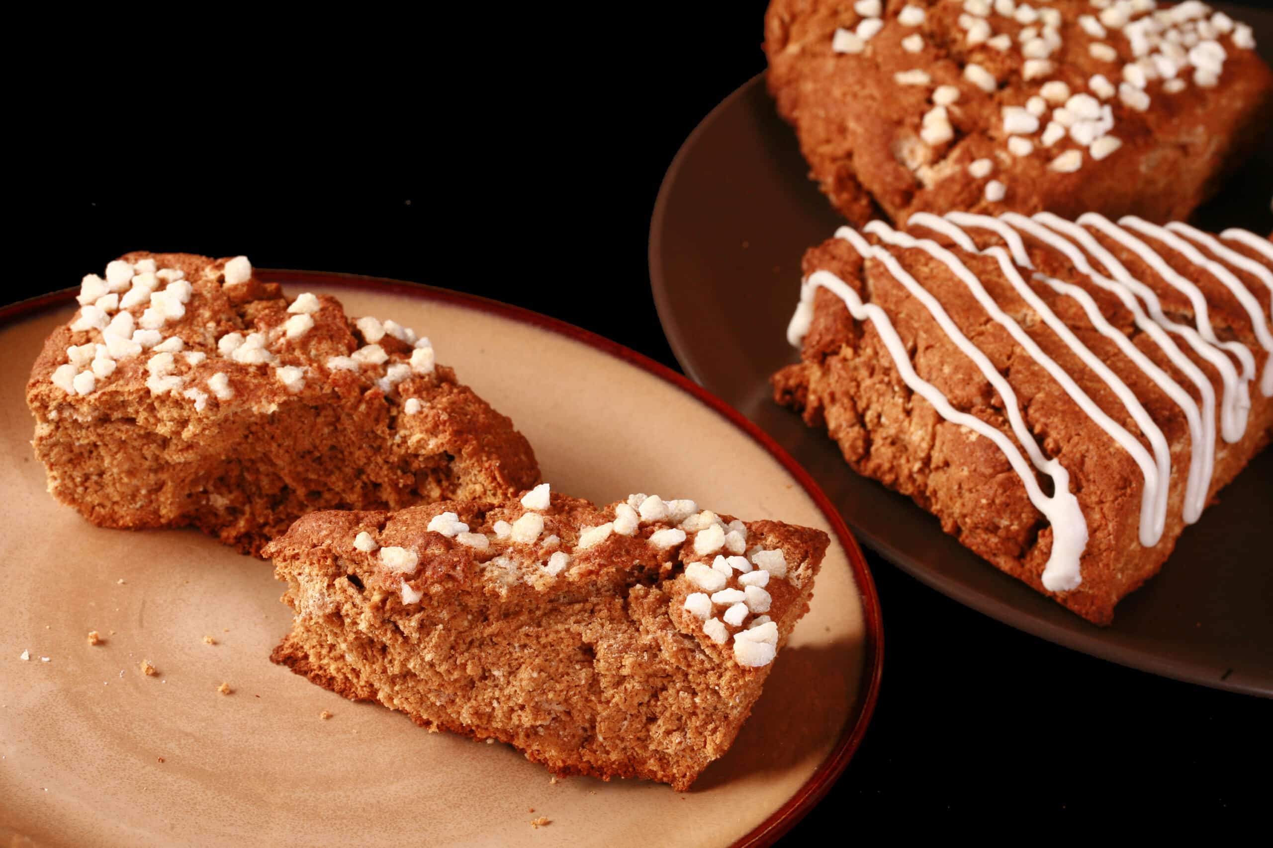 A plate of gluten free gingerbread scones. Half have a sugar crust, the other half have a vanilla glaze drizzled over them.