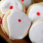Close up view of a plate of Gluten-Free Empire Cookies - sandwich cookies filled with raspberry jam, frosted with a white glaze, and finished off with a dot of red gel in the center.
