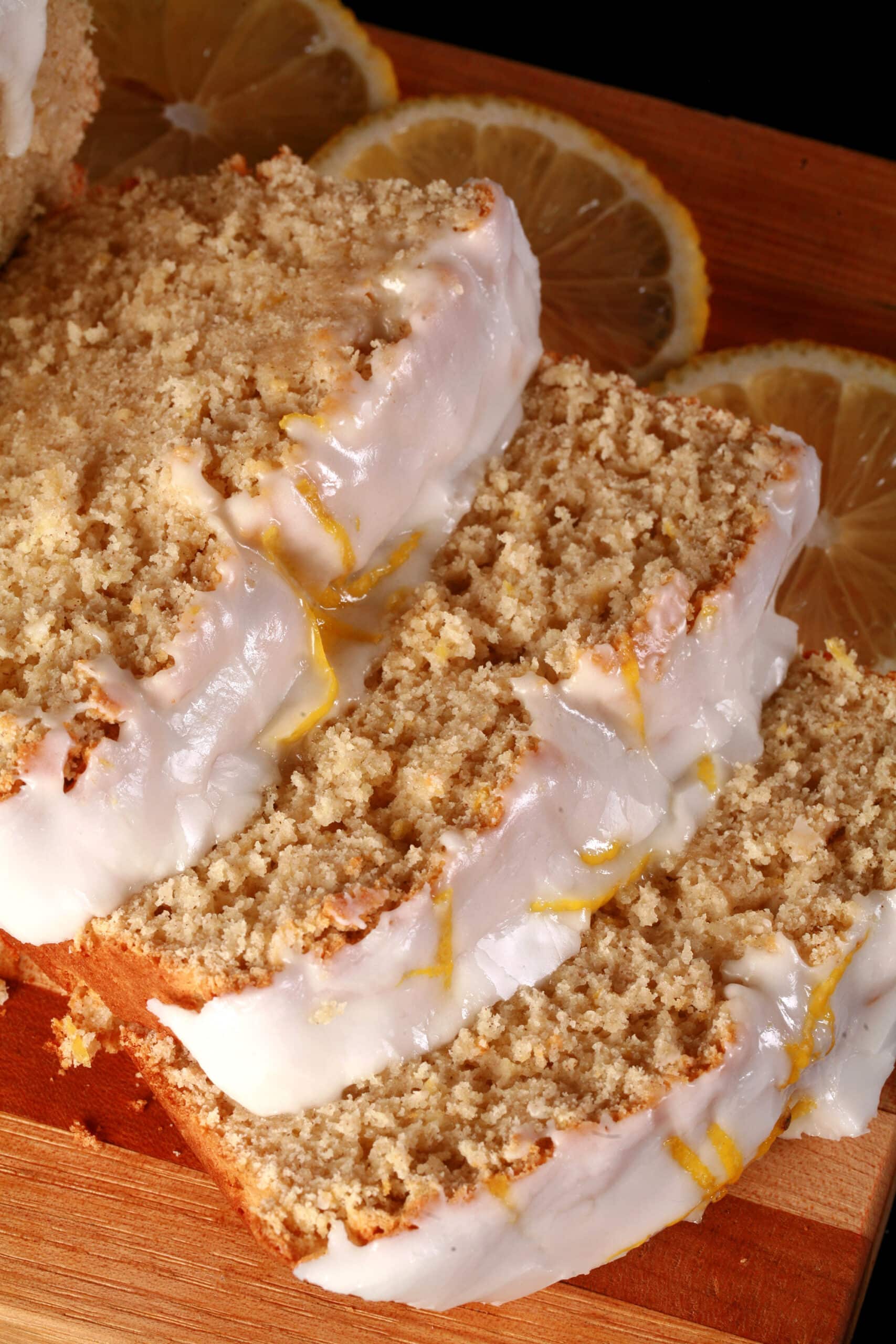 A sliced loaf of gluten-free lemon drizzle cake, with white glaze and lemon zest on top.