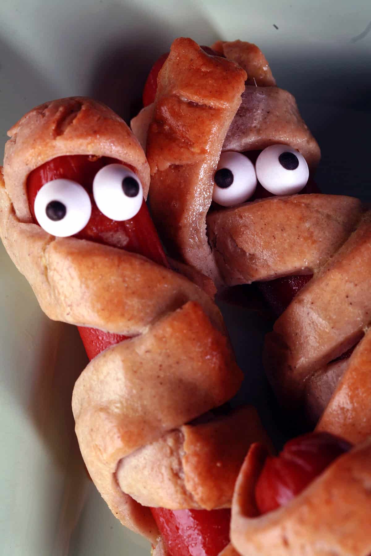 Several gluten-free mummy dogs on a plate. Each have 2 candy eyes.