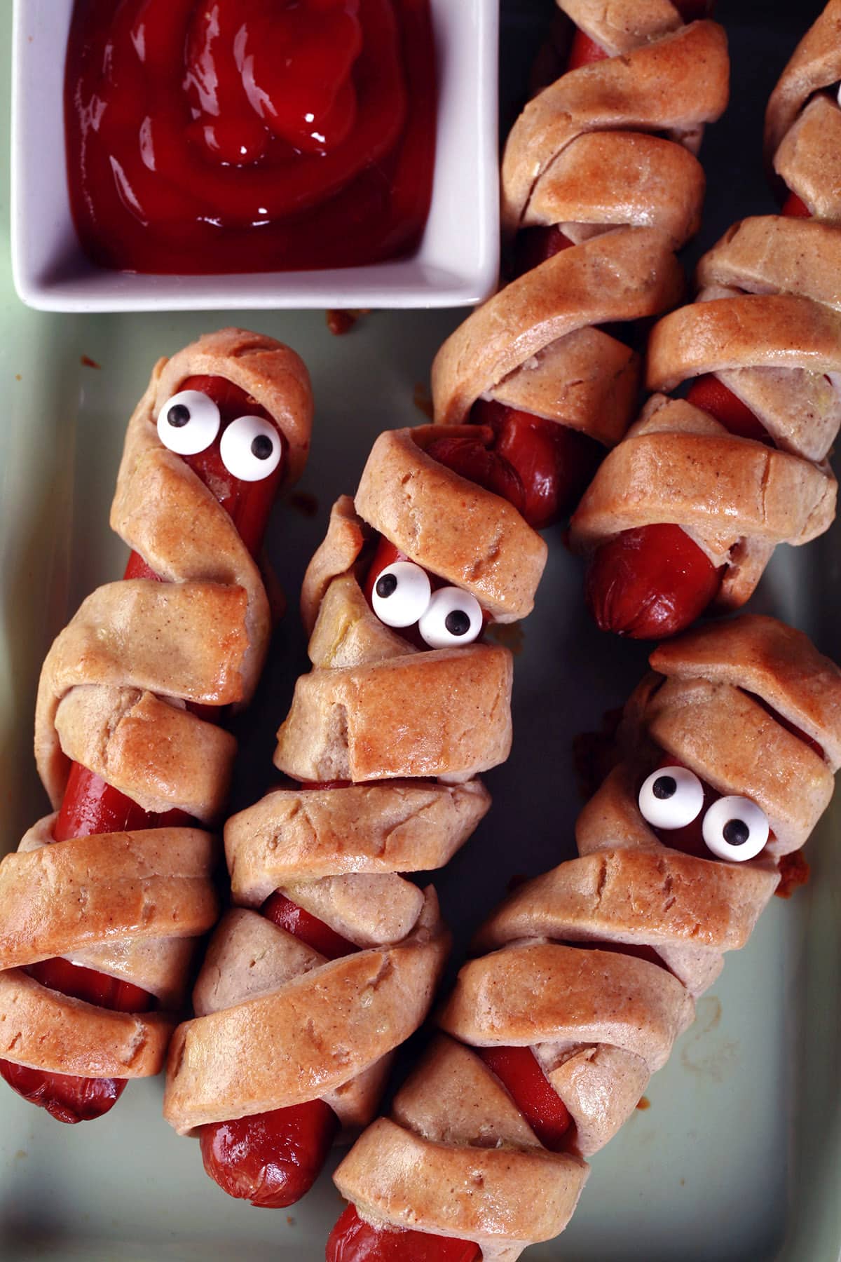 Several gluten-free mummy dogs on a plate. Each have 2 candy eyes.