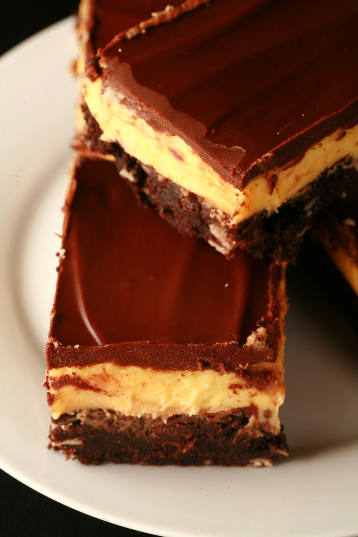 A plate of gluten-free Nanaimo Bar Brownies - A fudgey brownie, topped with a rich custard buttercream and a layer of chocolate ganache.