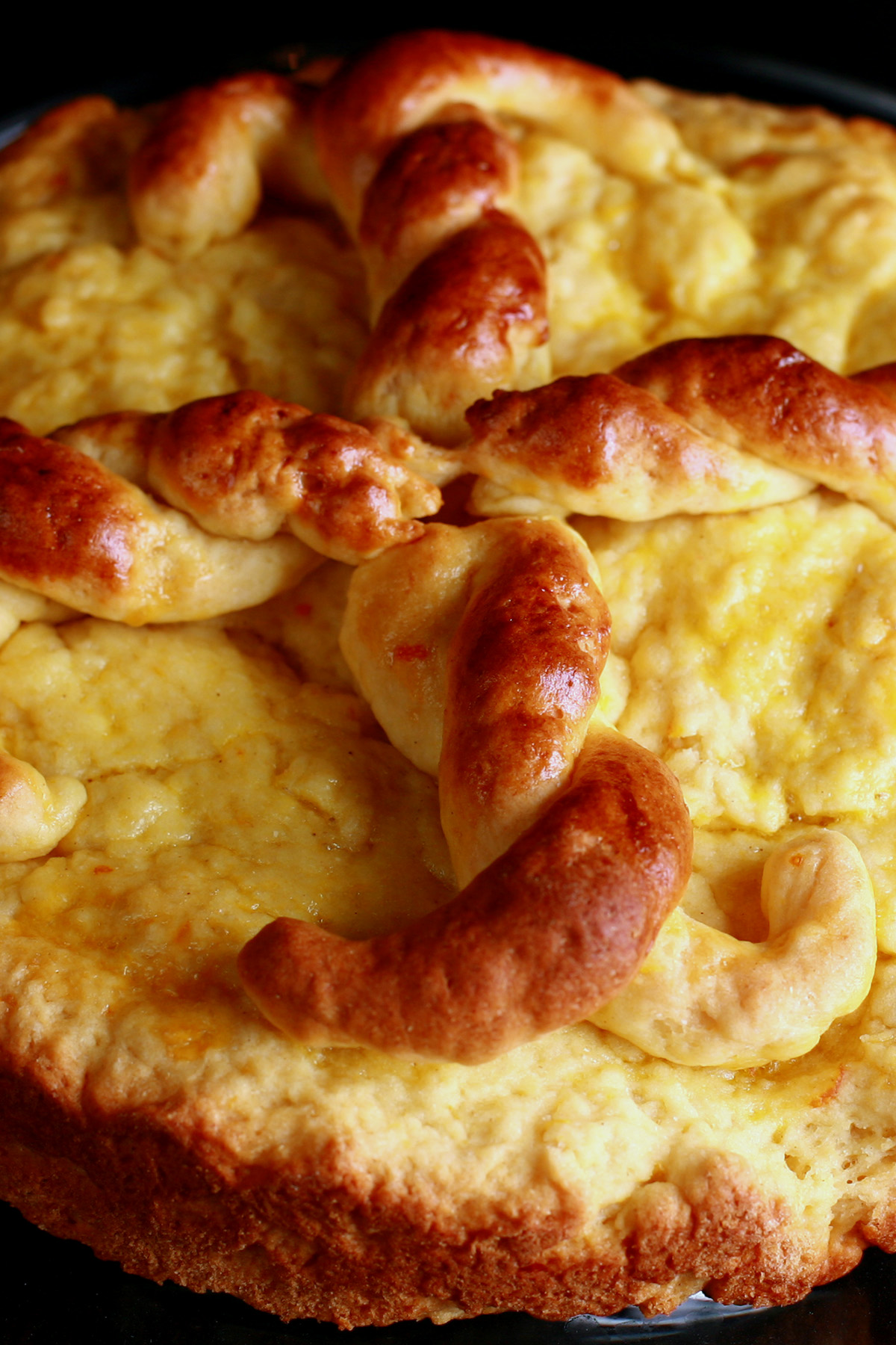 A pale yellow, flatish round of bread has a darker brown twisted design on top, made from bread dough.