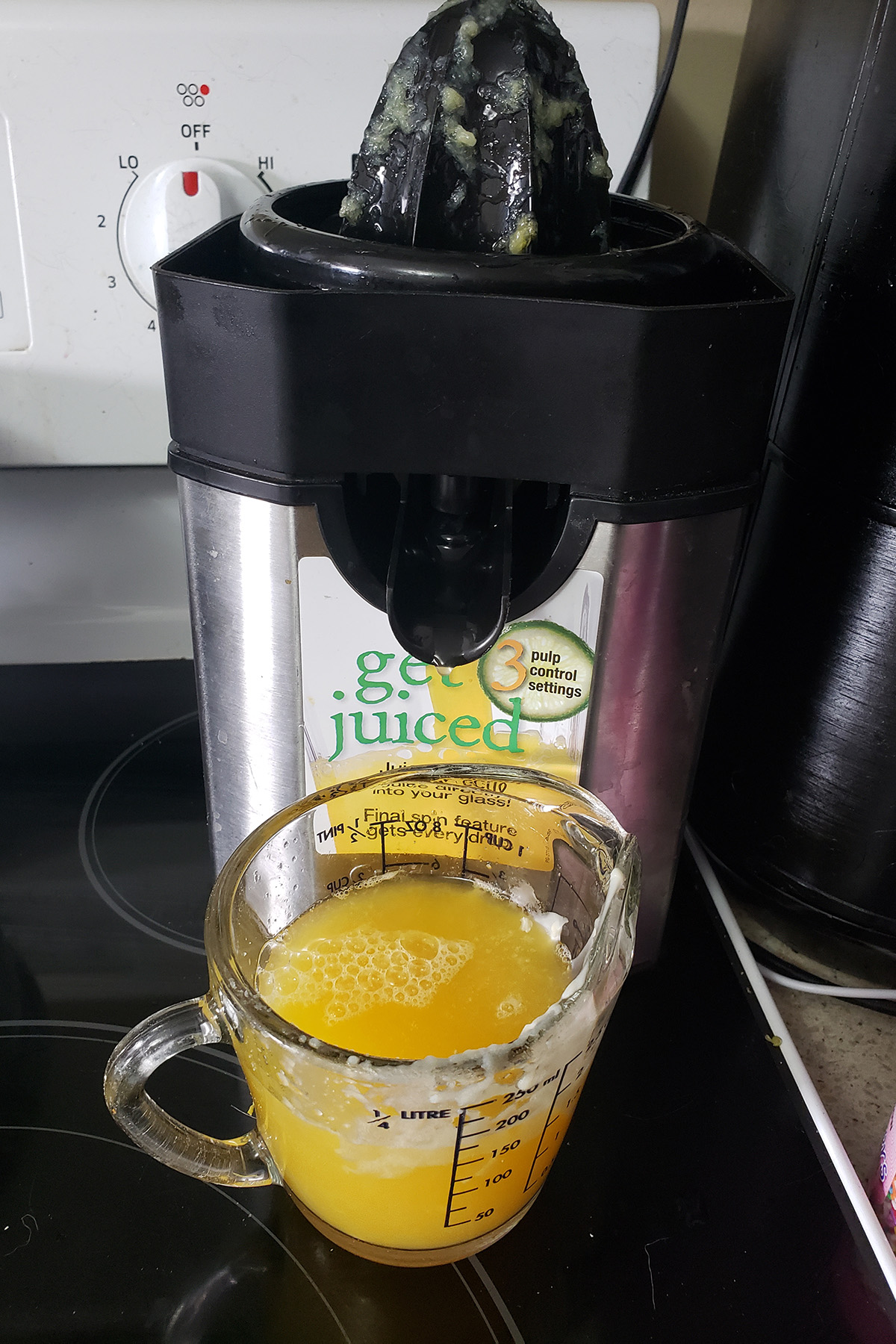 A measuring glass of juice sits in front of a juicing appliance.
